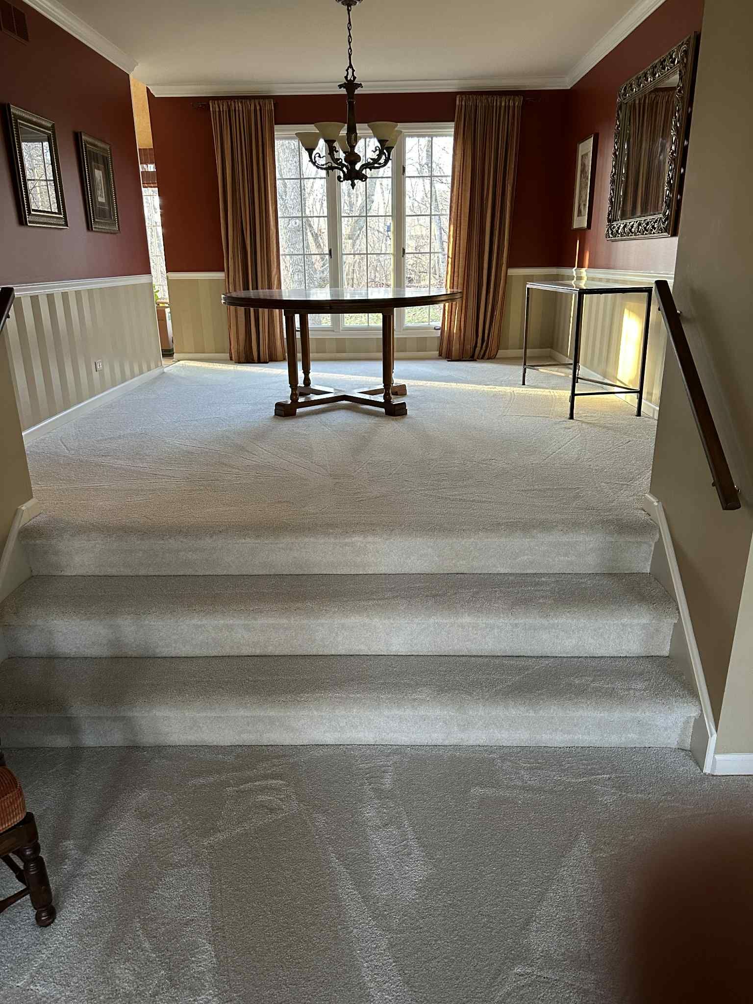 Carpeted stairs leading up to a large room with a table, windows, and red walls.