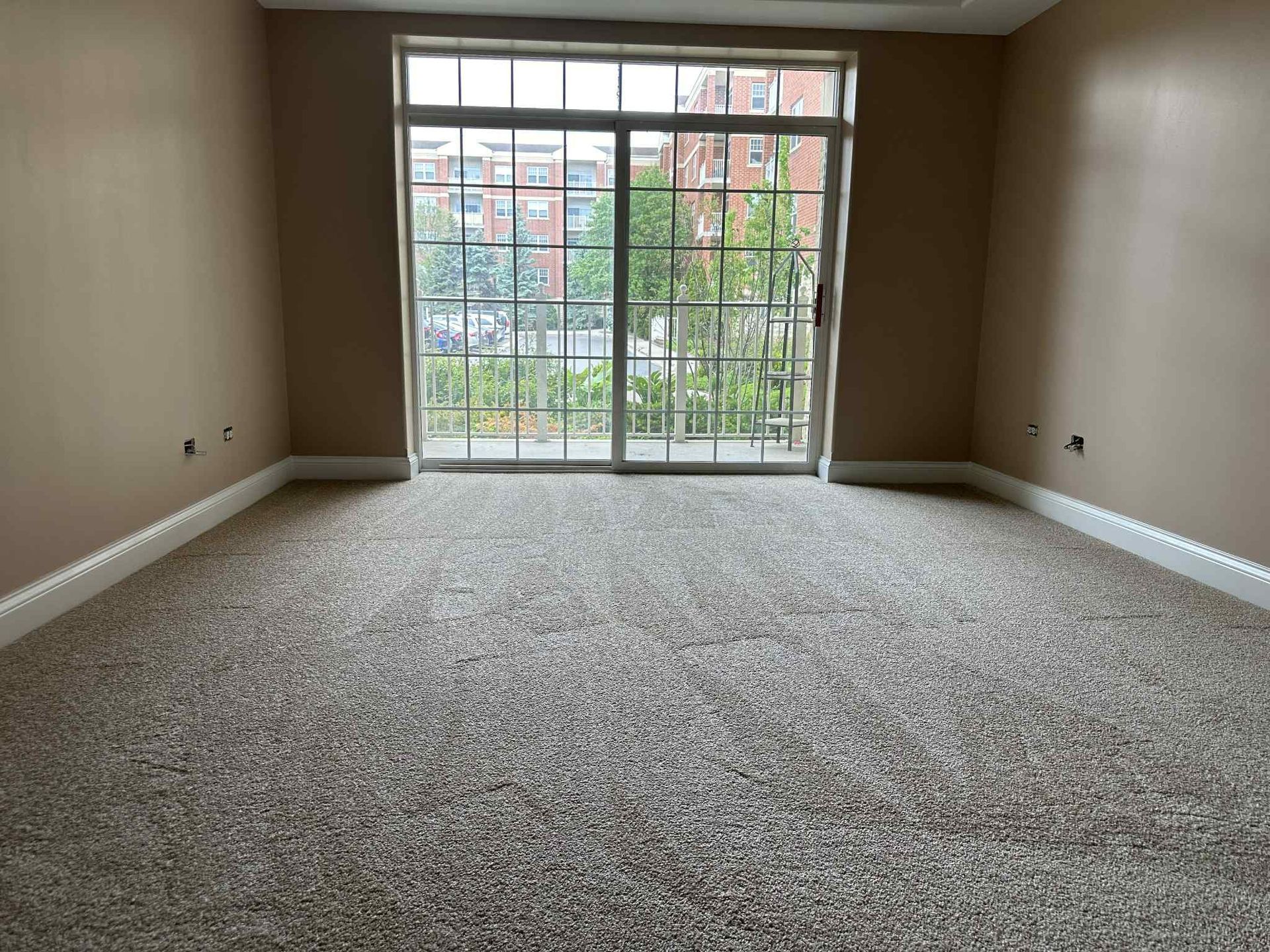 Empty room with beige walls, patterned carpet, and sliding glass door.
