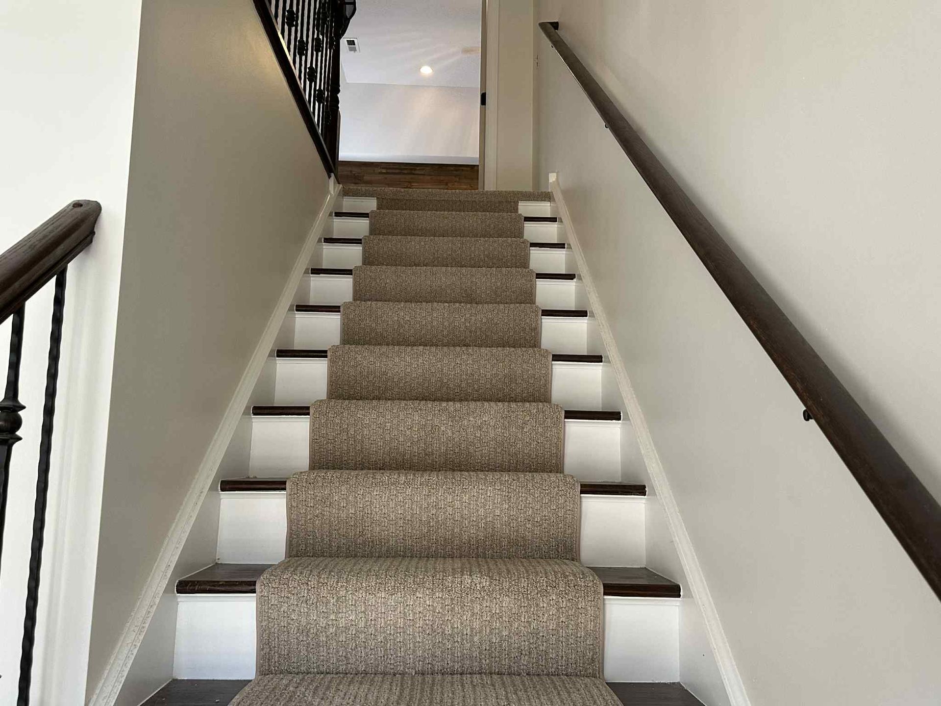 Staircase with carpet runner, white risers, and dark wood handrails ascending towards an open doorway.