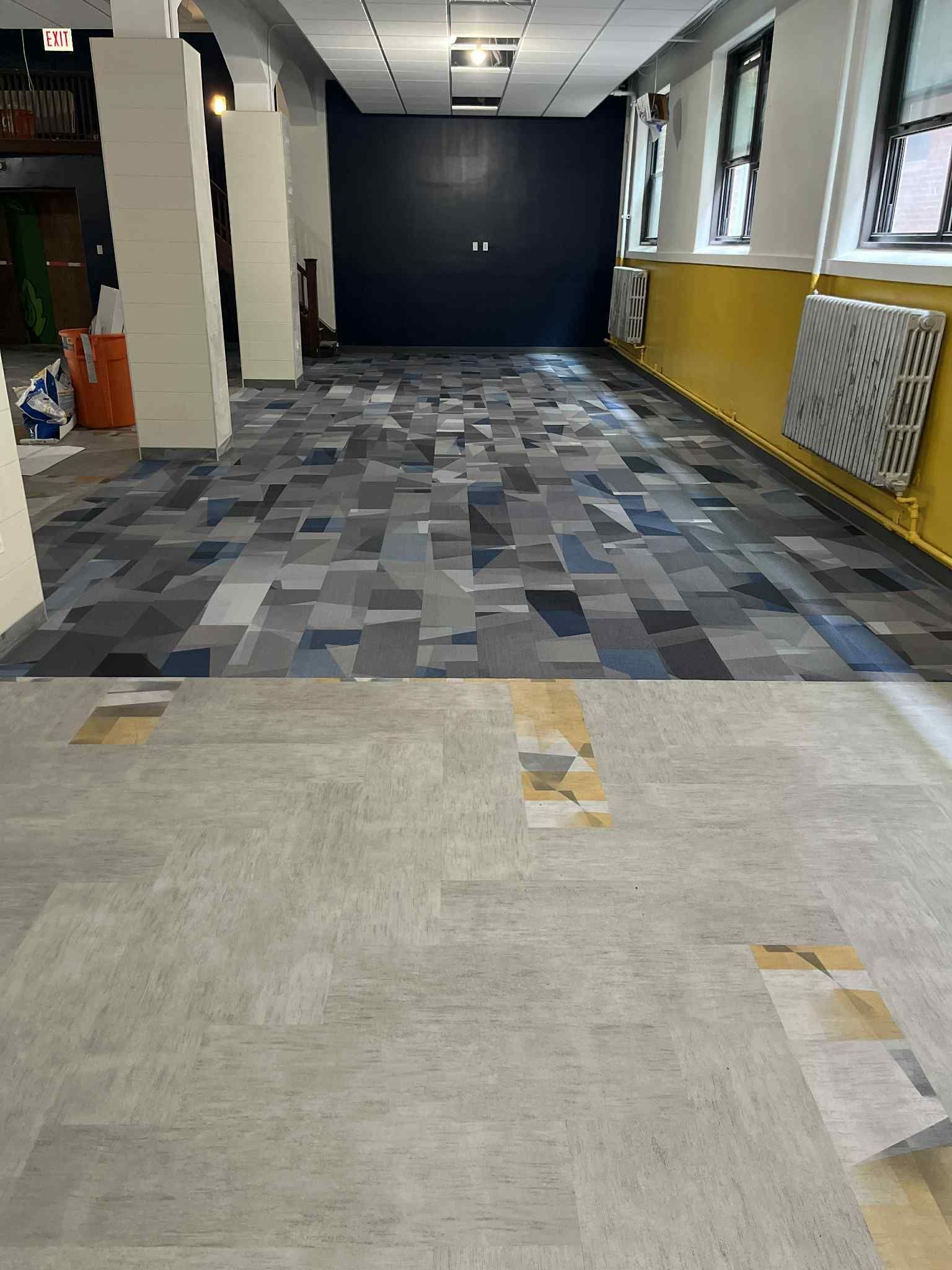 Room with two-toned floor: light gray and patterned blue. Yellow wall, dark blue wall in background.