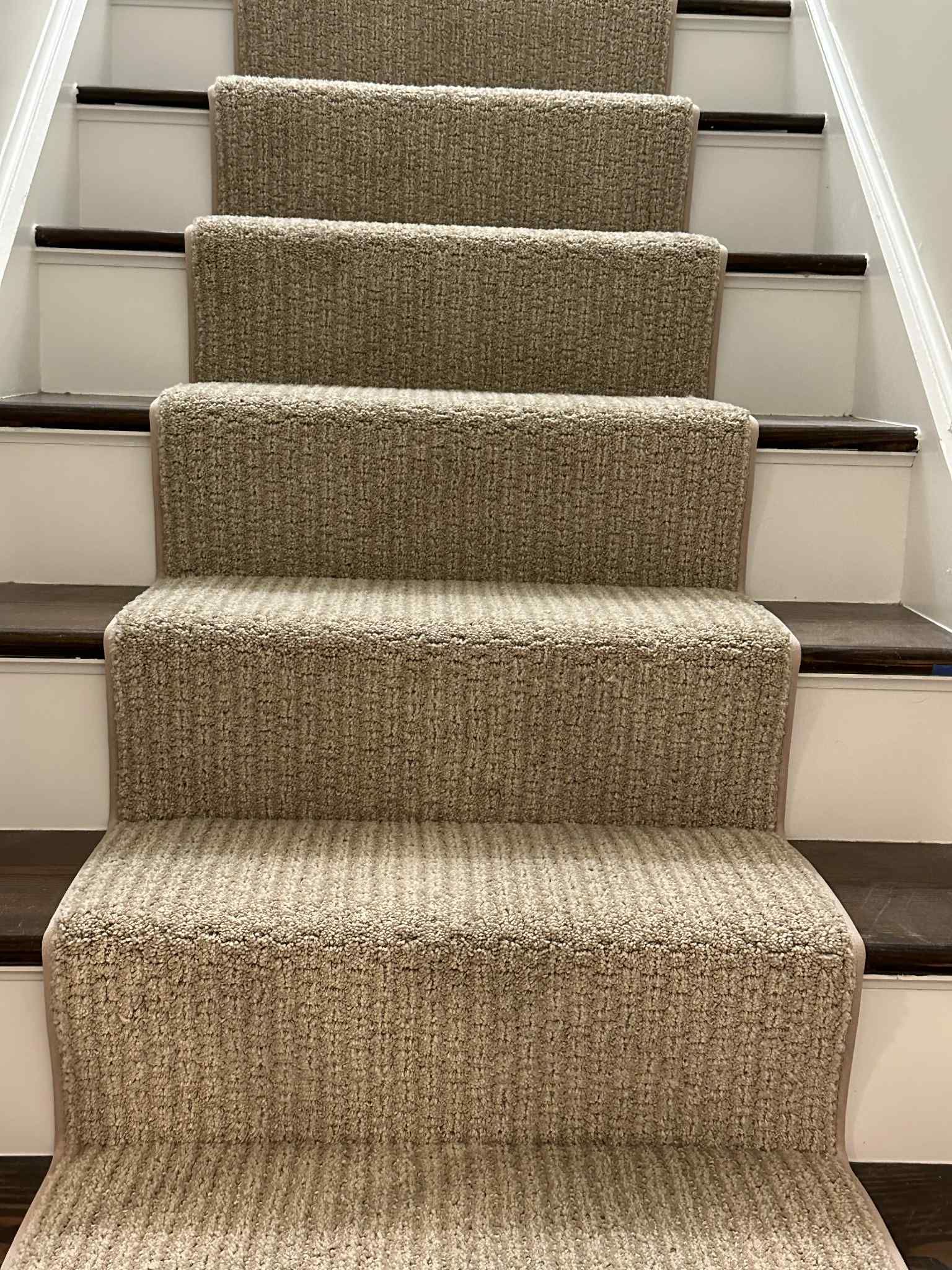Carpeted staircase with light brown and beige tones. The steps are covered in a looped carpet. Dark wood and white trim.