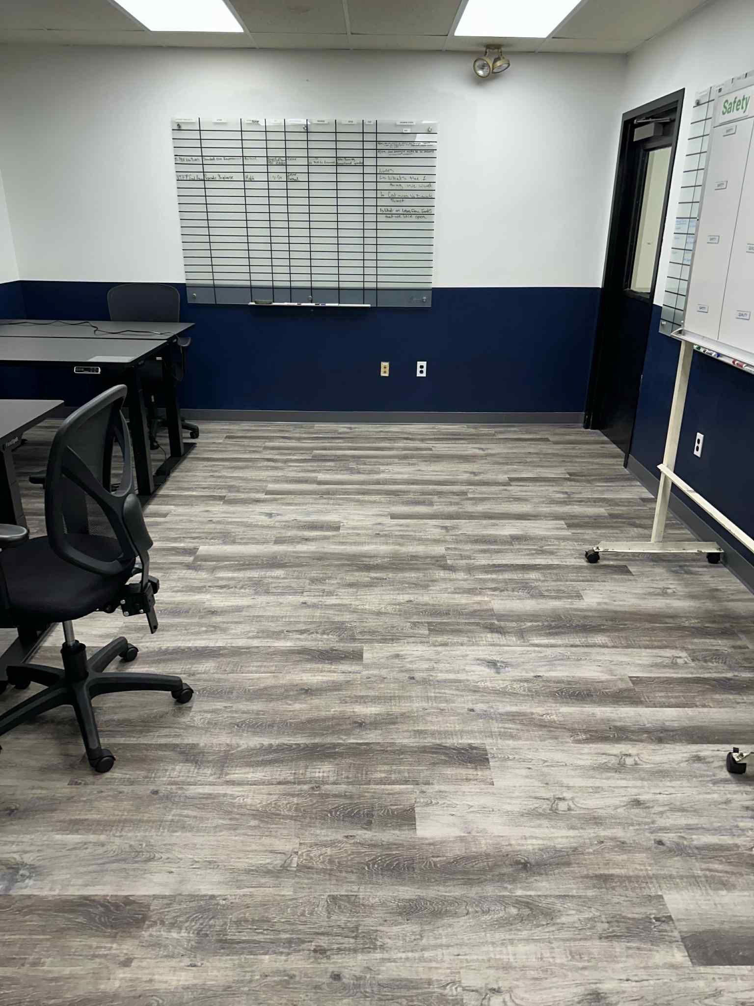 An office room with wooden floors, white walls, and navy blue accents. A whiteboard and desk with a chair are present.