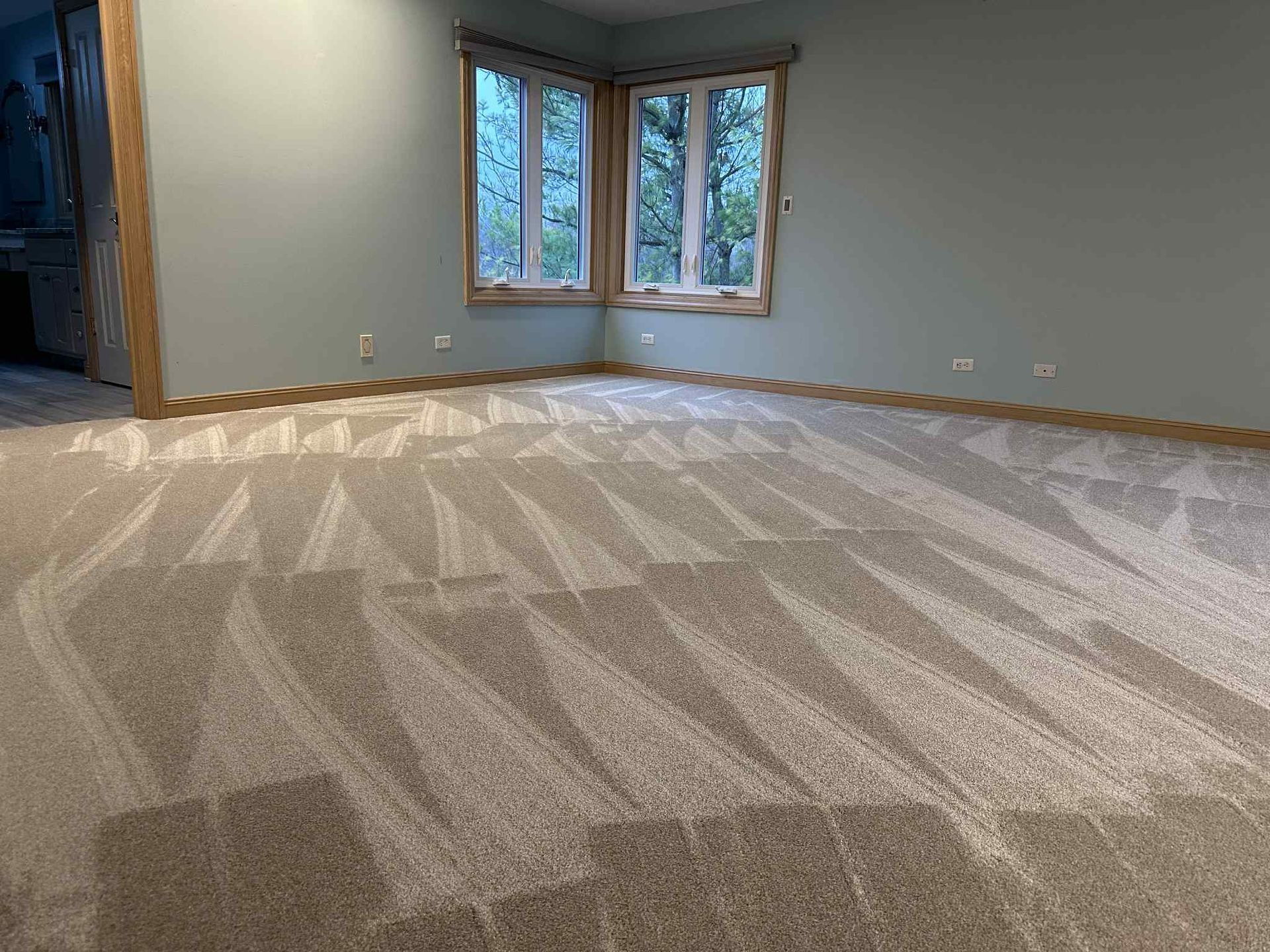 Beige carpeted room with light blue walls, a corner window, and wood trim.