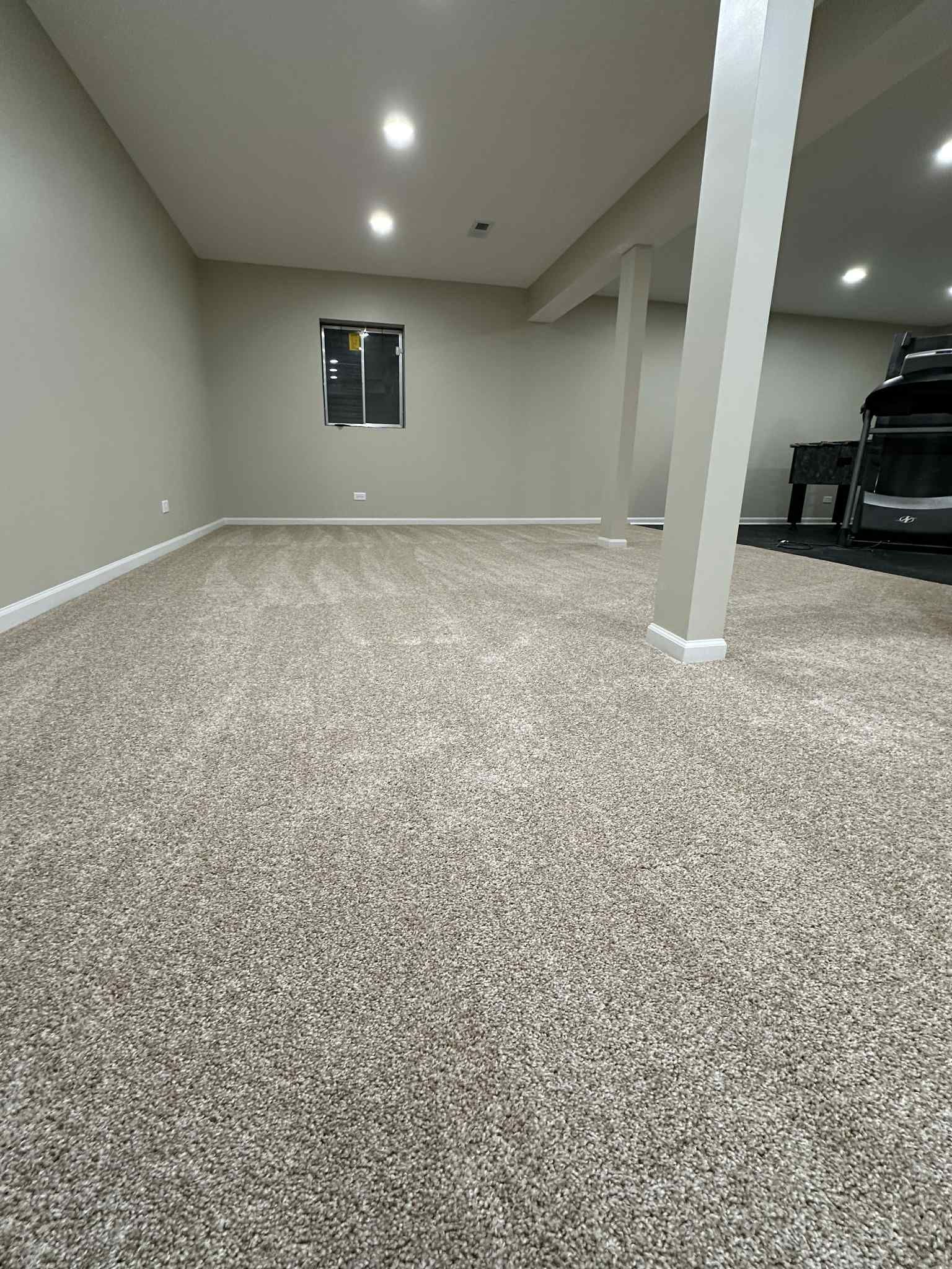 Empty finished basement with neutral walls, carpet, and support beams.