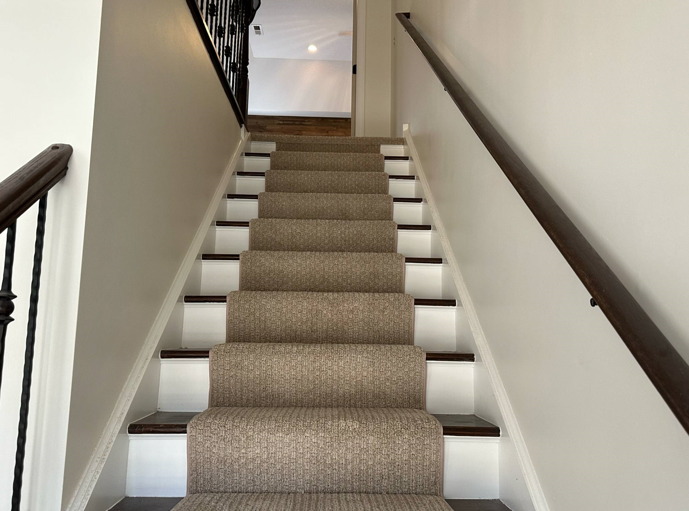Staircase with carpeted steps and white risers leading to an open doorway. Handrails on both sides.
