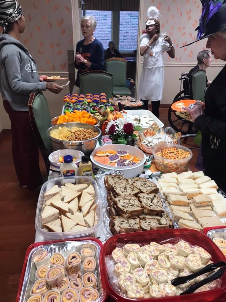 A buffet table with various snacks, people in a room, and a woman in a costume.