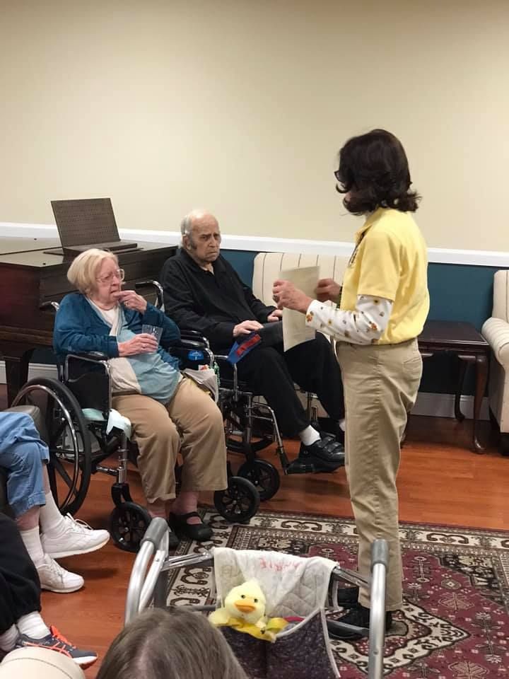 Person in yellow shirt speaks to two people in wheelchairs. Interior setting.