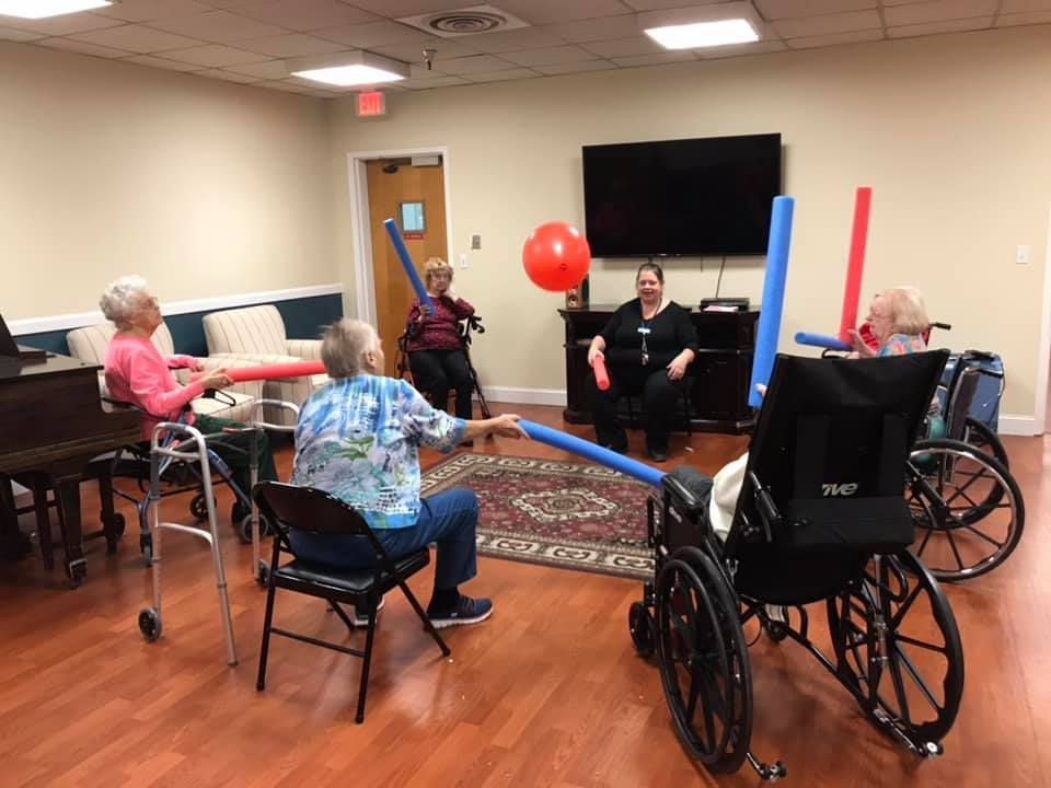 Seniors in a group exercise class using pool noodles and a red balloon.