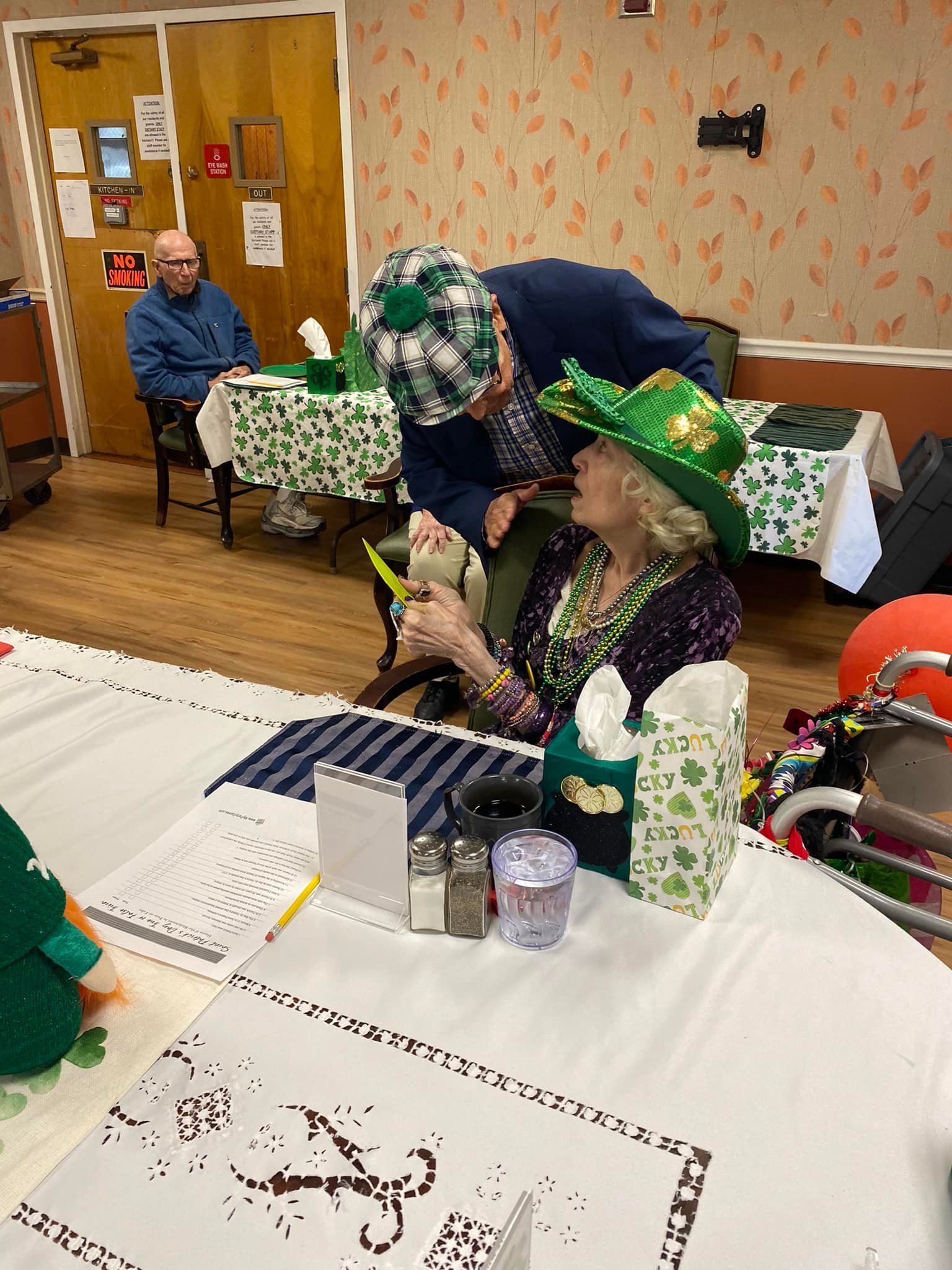 Two people in St. Patrick's Day hats near a table with decorations, another person in the background.