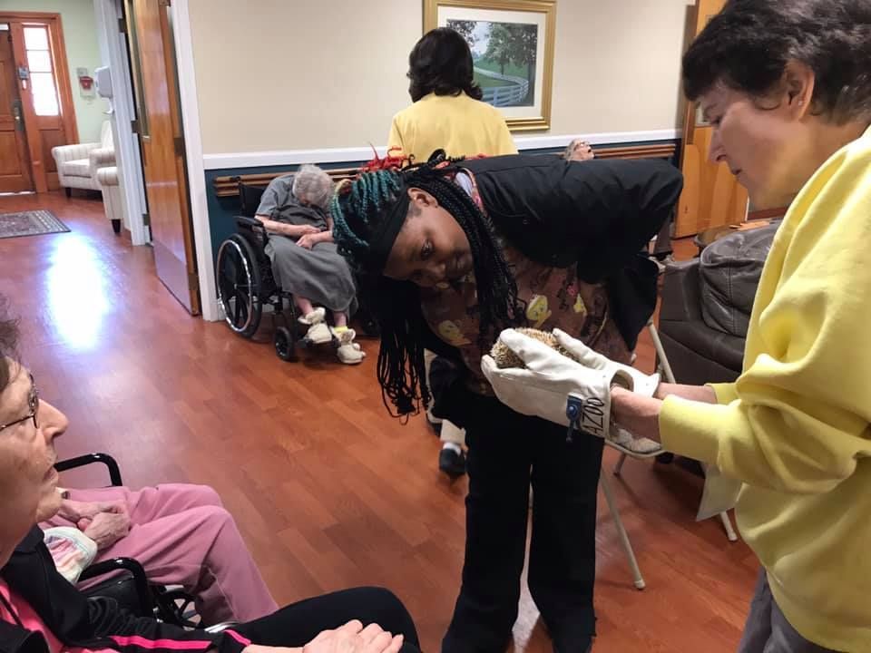 People in a nursing home setting. One person assists another wearing a mitt, others watch.