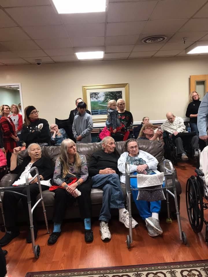 People seated on a couch and standing in a room, some with walkers.