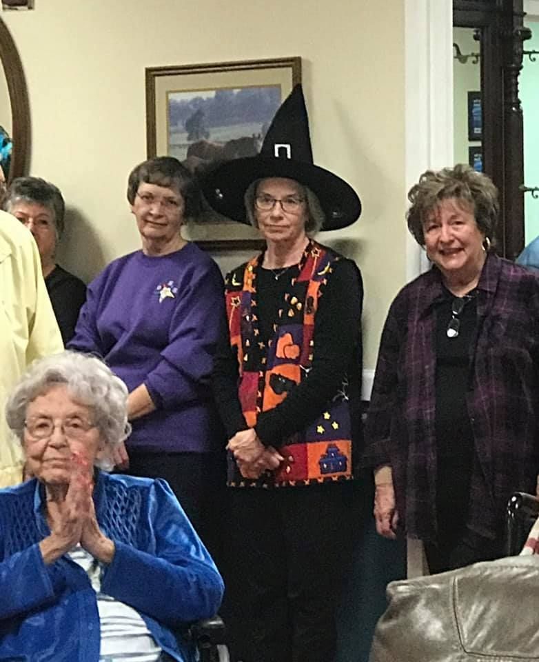 Group of people, one in a witch hat, gathered indoors.