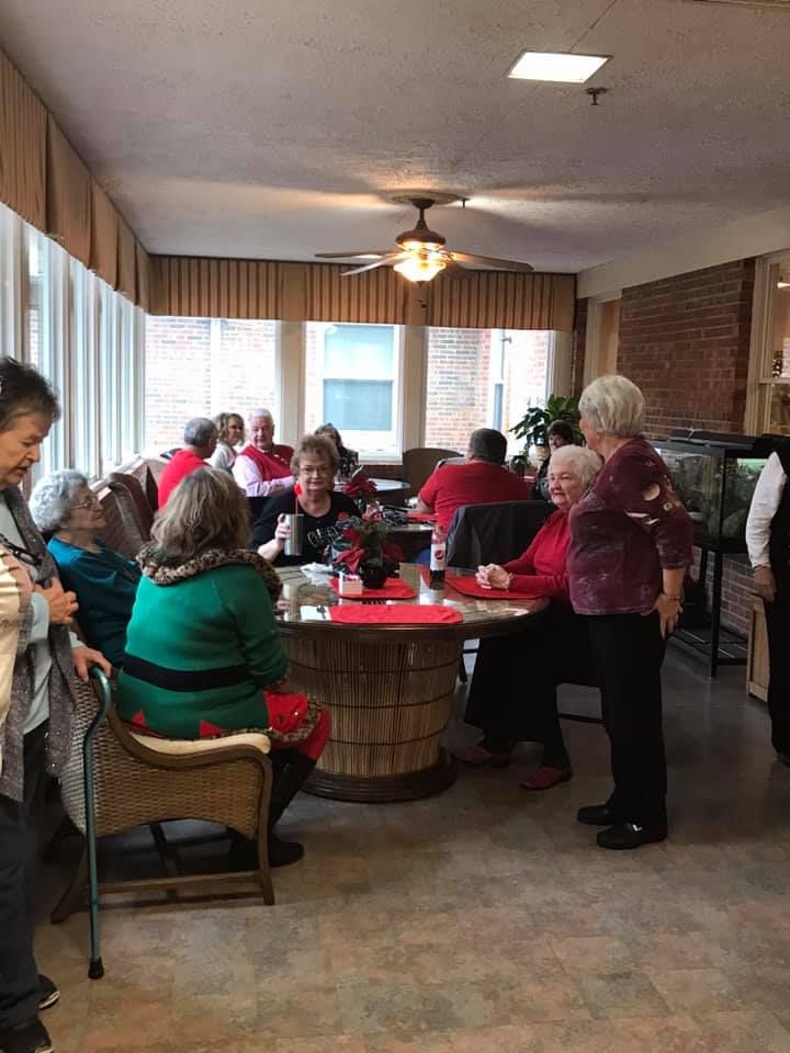 People seated at round tables in a brightly lit room, some wearing red tops.