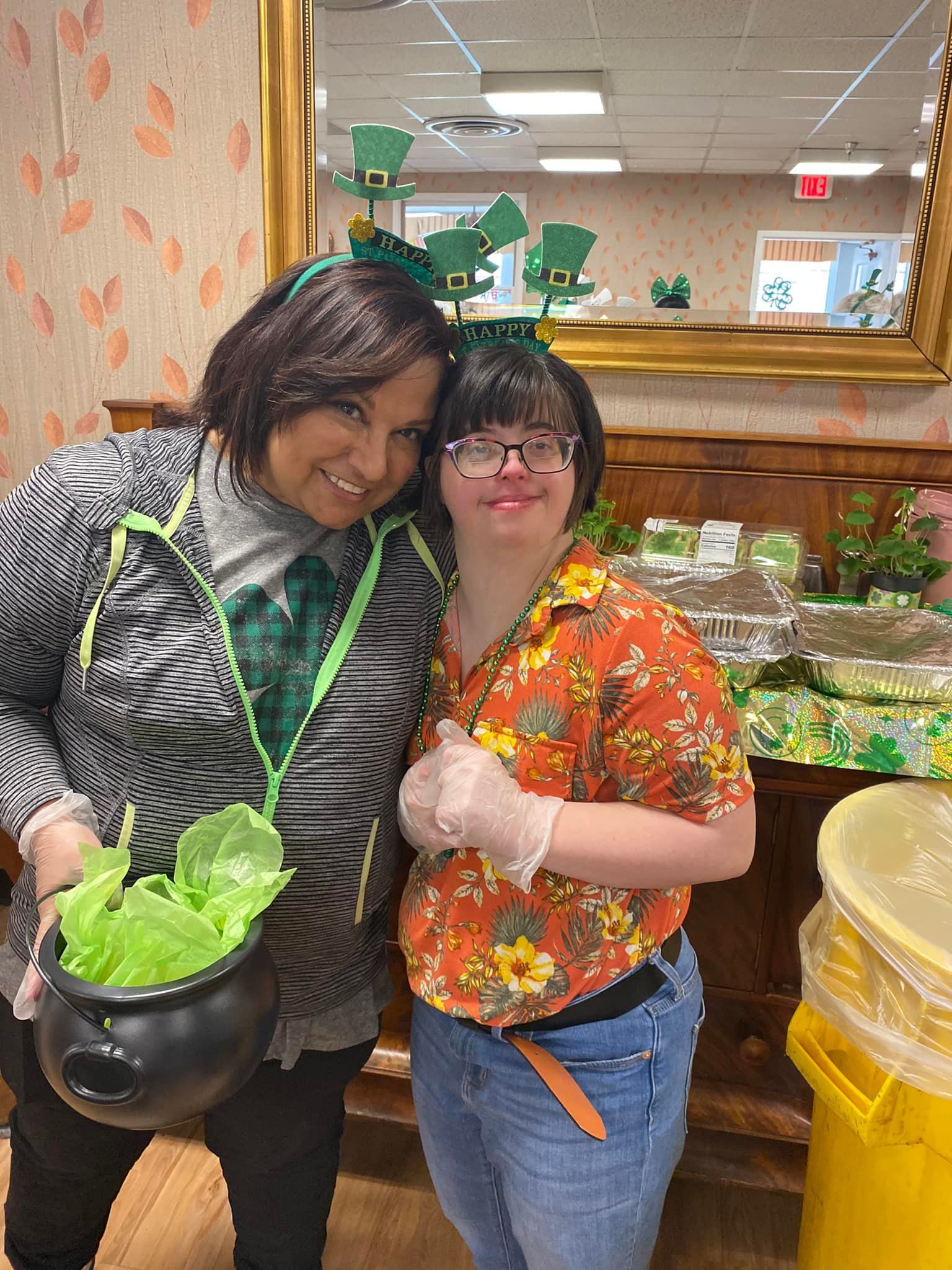 Two people with St. Patrick's Day headbands smile near a buffet. One holds a pot of lettuce.