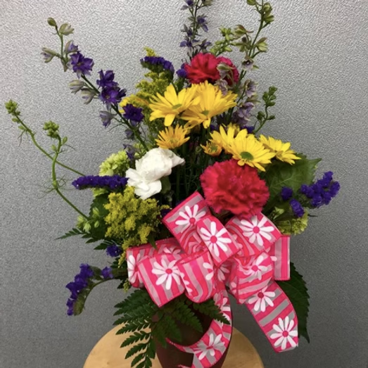 Colorful flower arrangement in a vase, with a pink daisy ribbon.