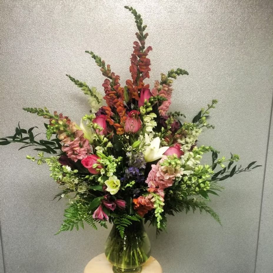 Vase of colorful flowers, including roses and snapdragons, on a light background.