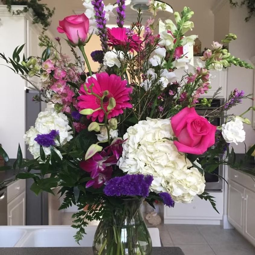 Colorful bouquet of pink, purple, and white flowers in a glass vase on a countertop.