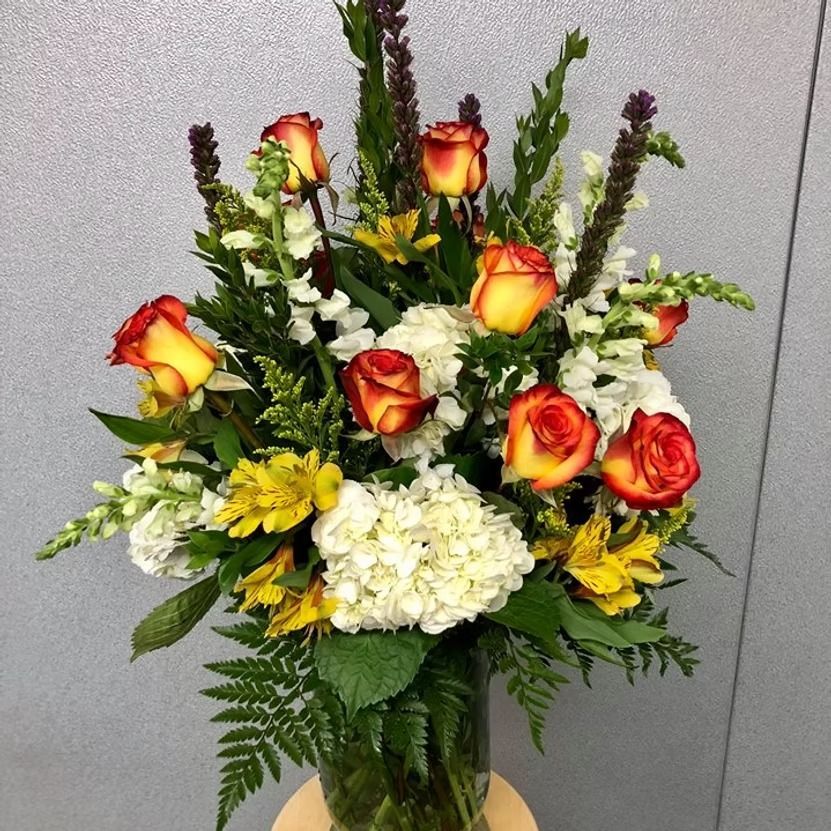Bouquet of orange roses, white hydrangea, and yellow flowers in a clear vase.