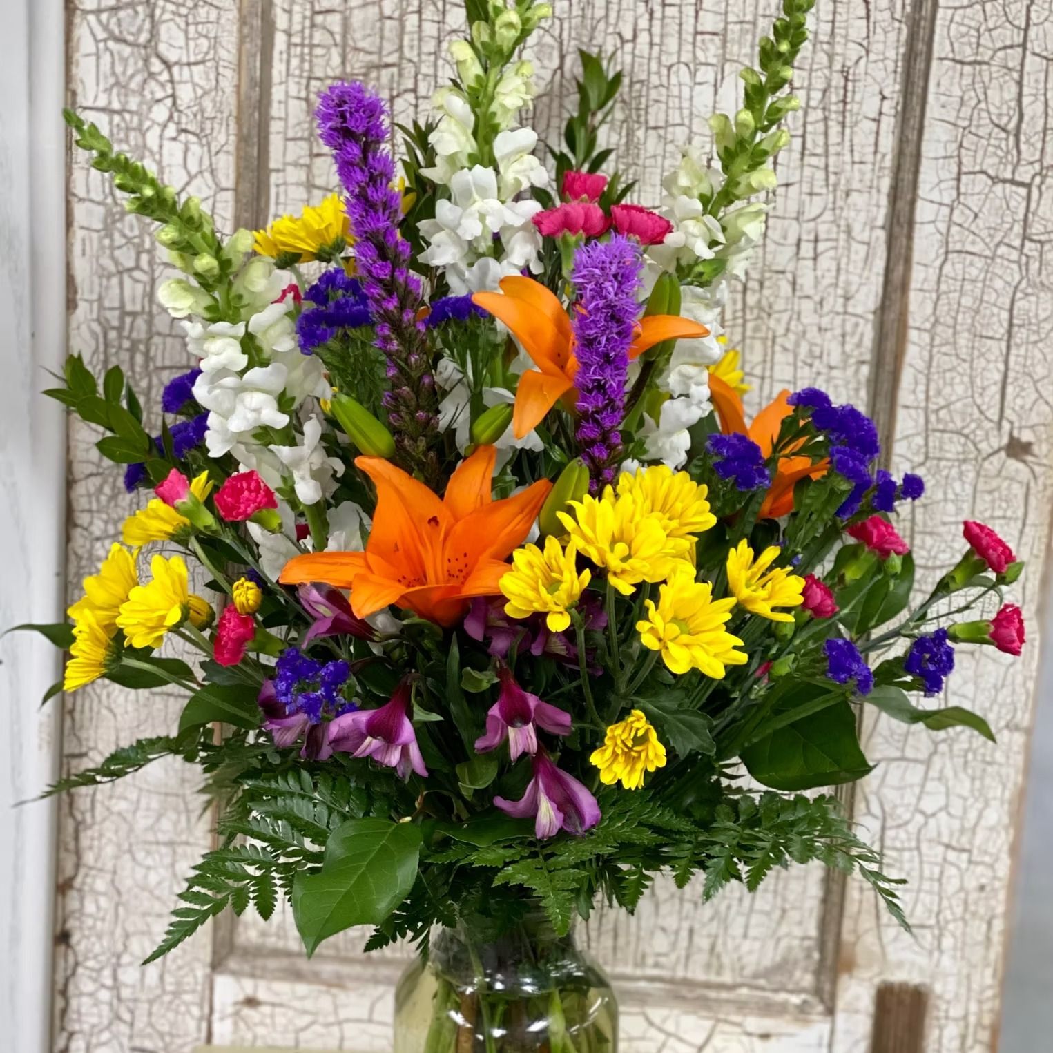 Colorful flower bouquet in a clear glass vase against a weathered wood background.