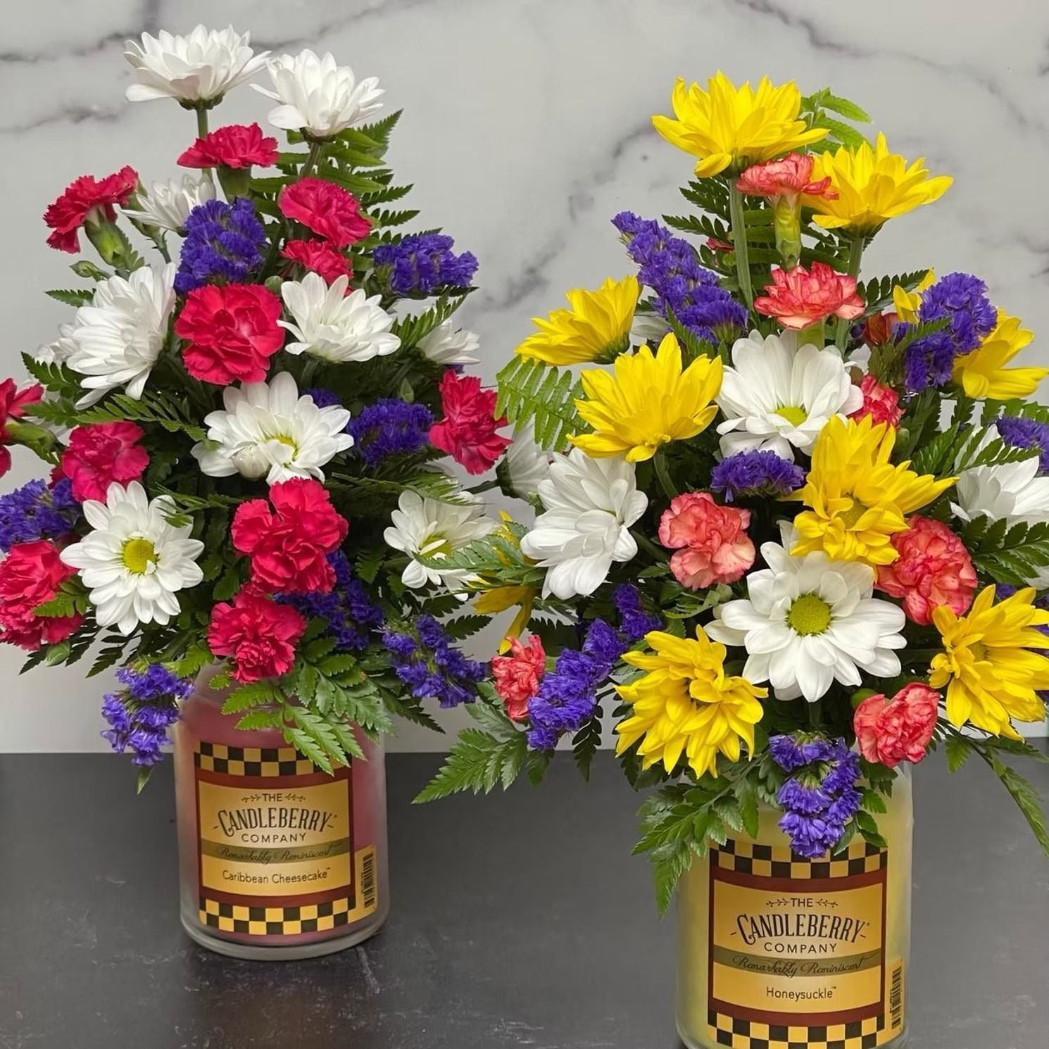Two colorful floral arrangements in cylindrical containers.