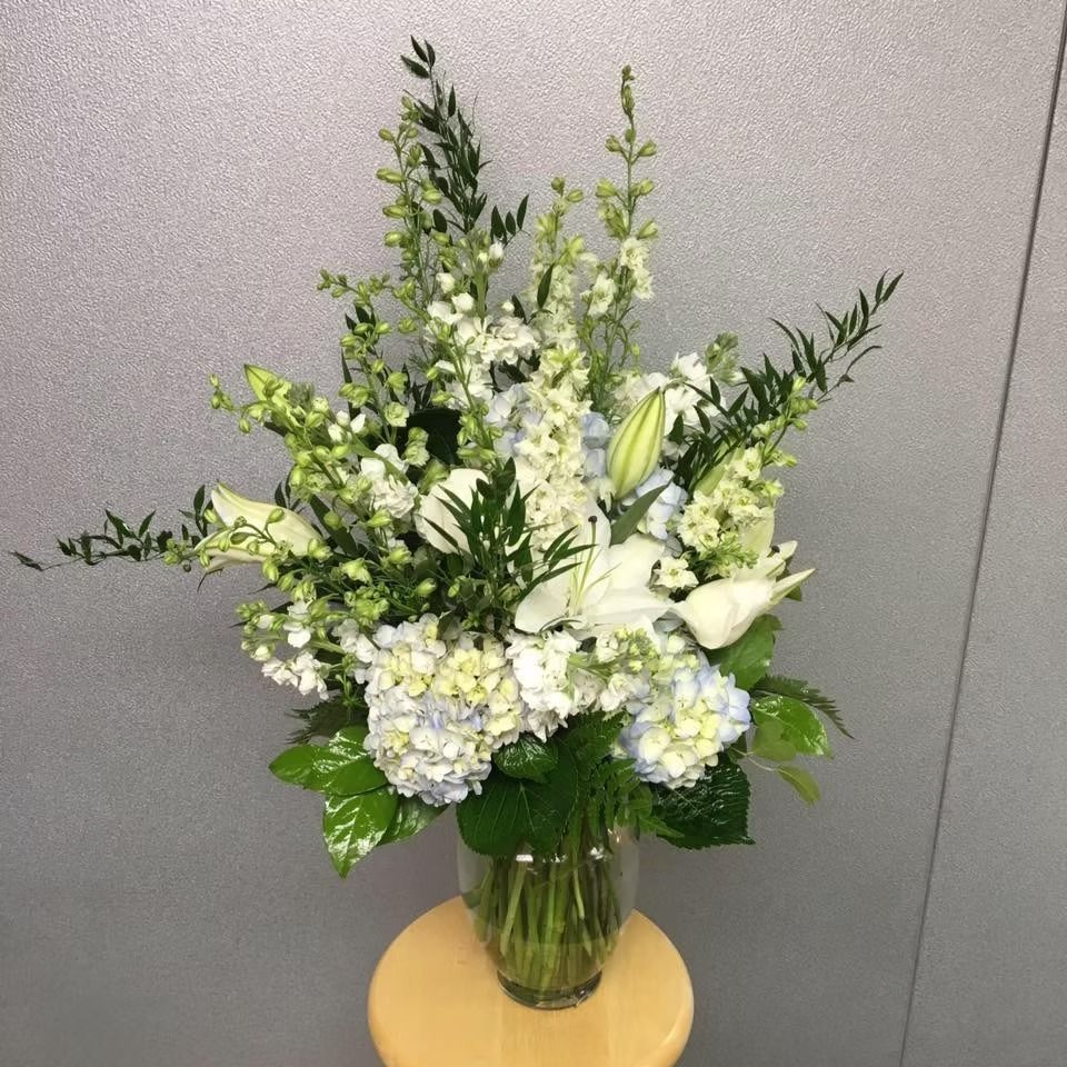 White and blue floral arrangement in a clear glass vase on a wooden stool.