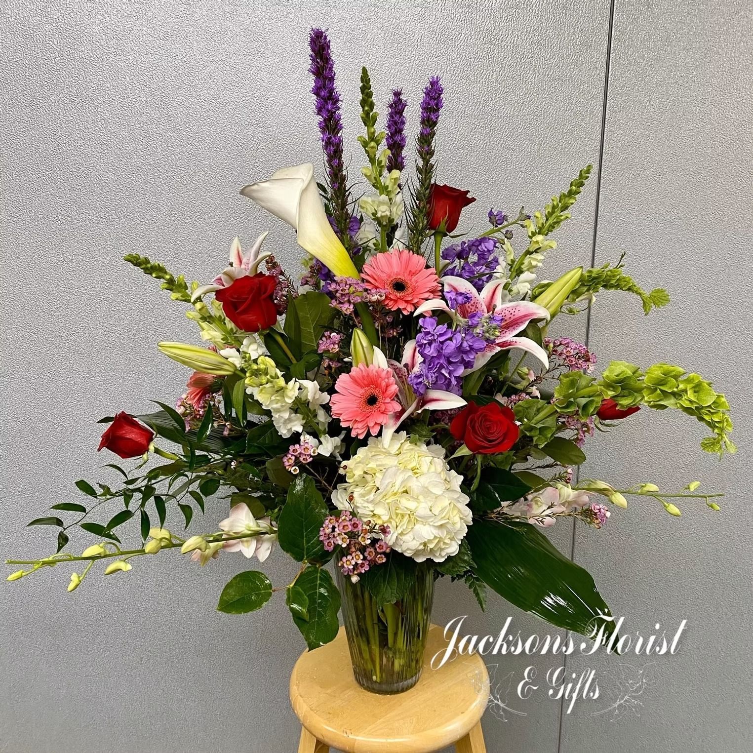 Floral arrangement in glass vase with assorted colorful flowers on wooden stool.