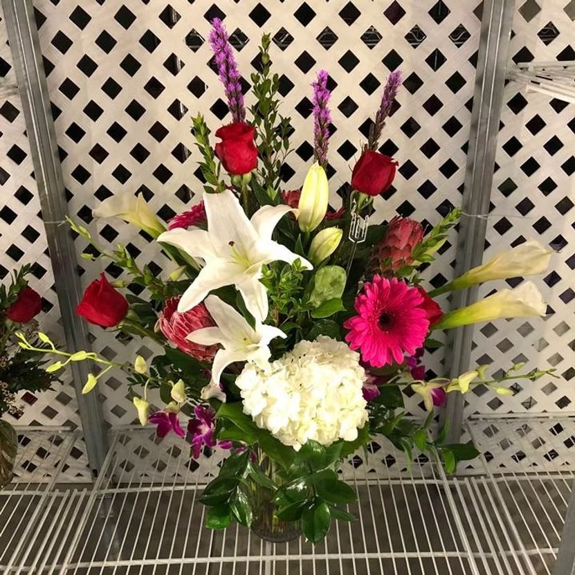 Floral arrangement with red roses, white lilies, pink gerbera daisies, and purple accents.