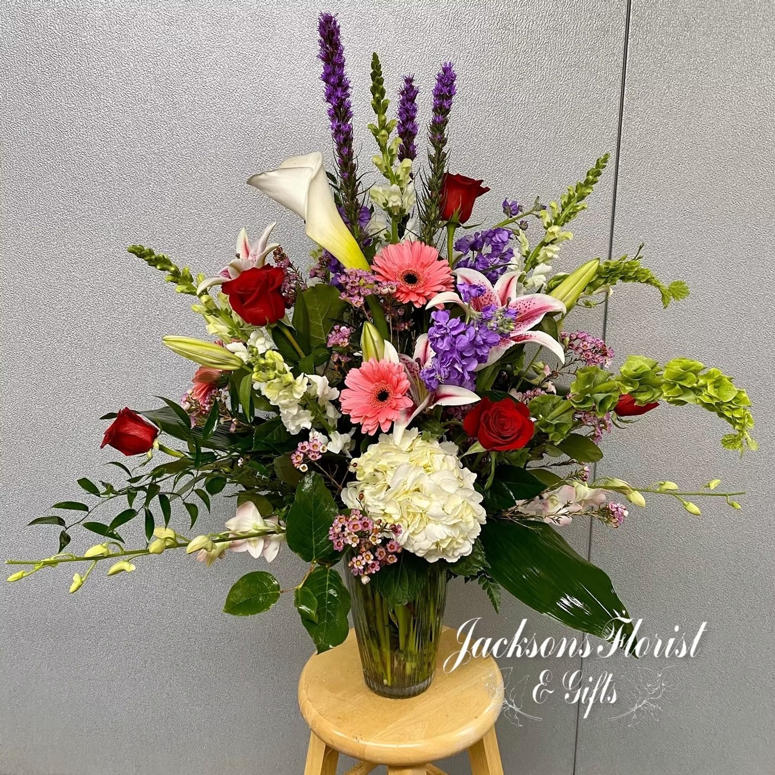 Floral arrangement in a glass vase; includes lilies, roses, and other colorful flowers.
