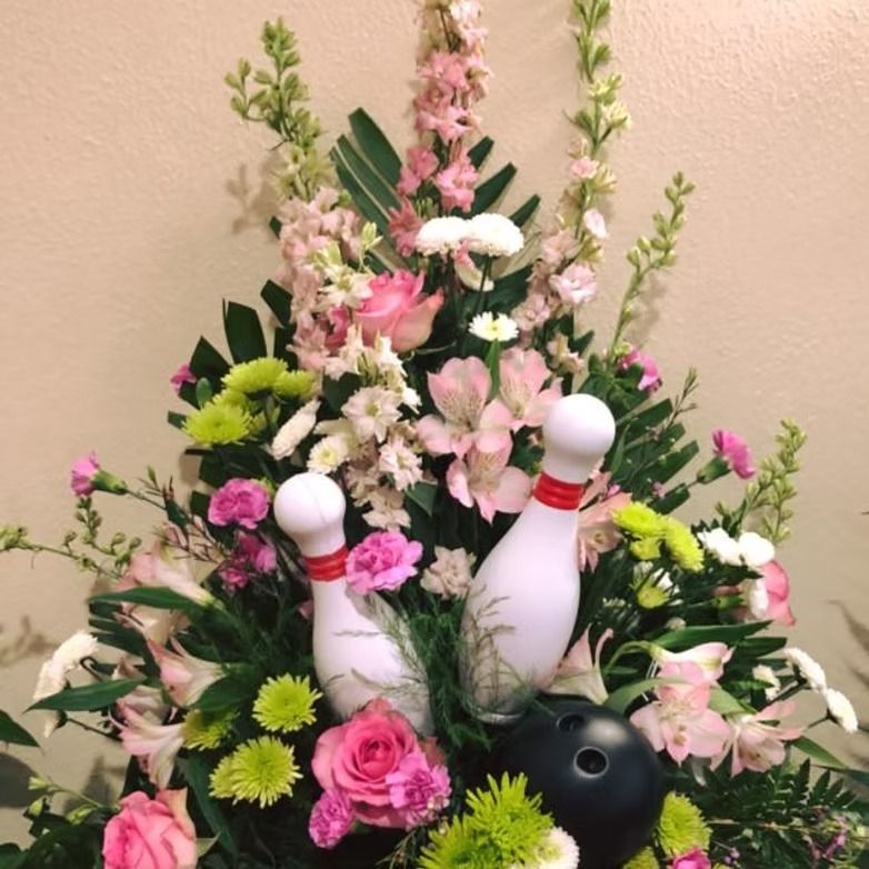 Floral arrangement with bowling pins and ball; pink, white, green flowers.