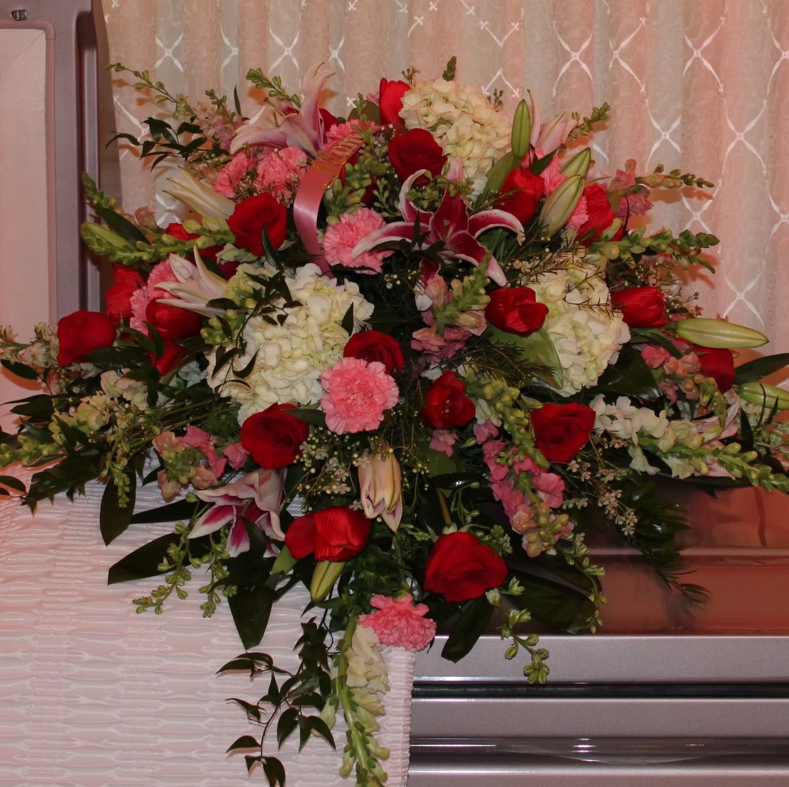 Floral arrangement with red roses, pink lilies, white hydrangeas, and greenery.