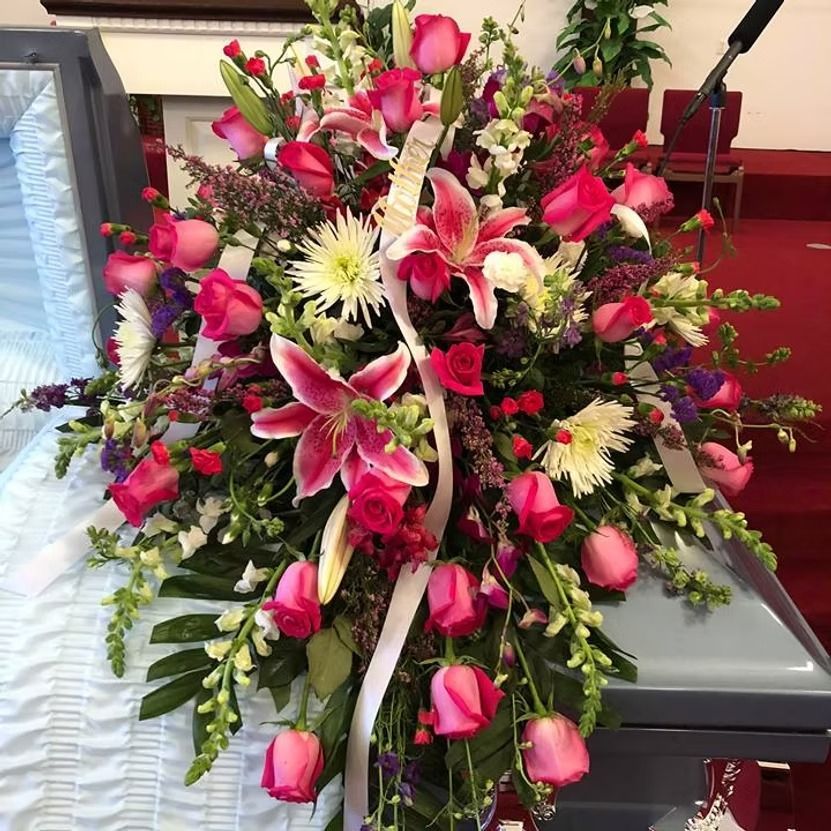 Floral arrangement of pink roses and lilies draped over a casket.