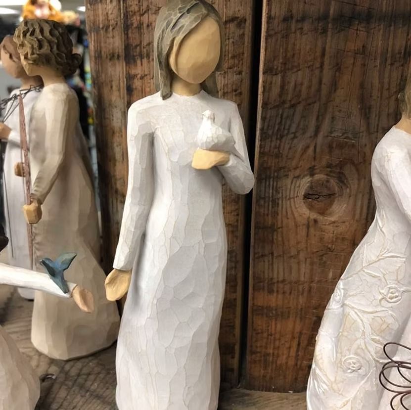 Statue of a woman in a white dress holding a dove, wooden background.