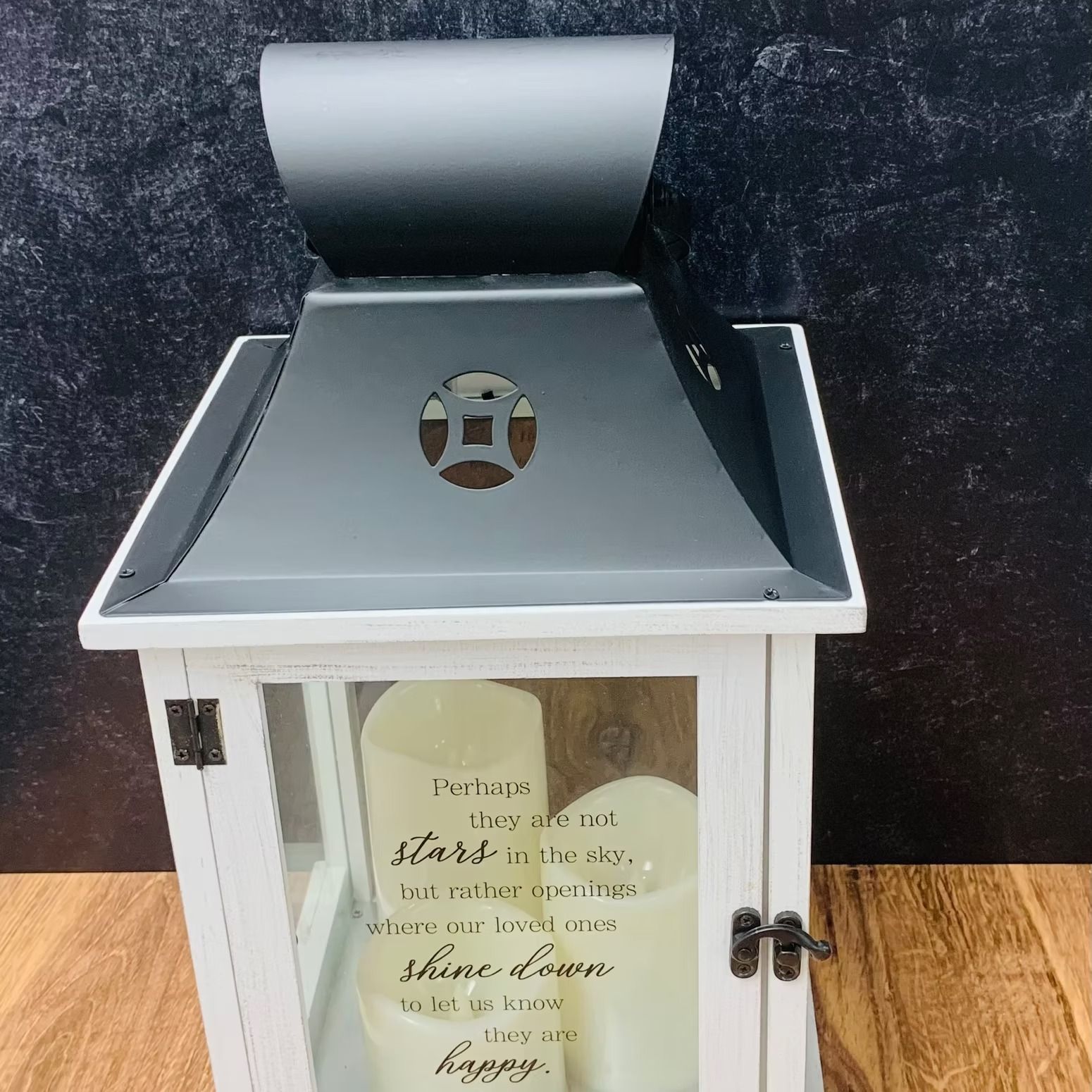 White lantern with a black top and a message about stars and happiness, containing candles.