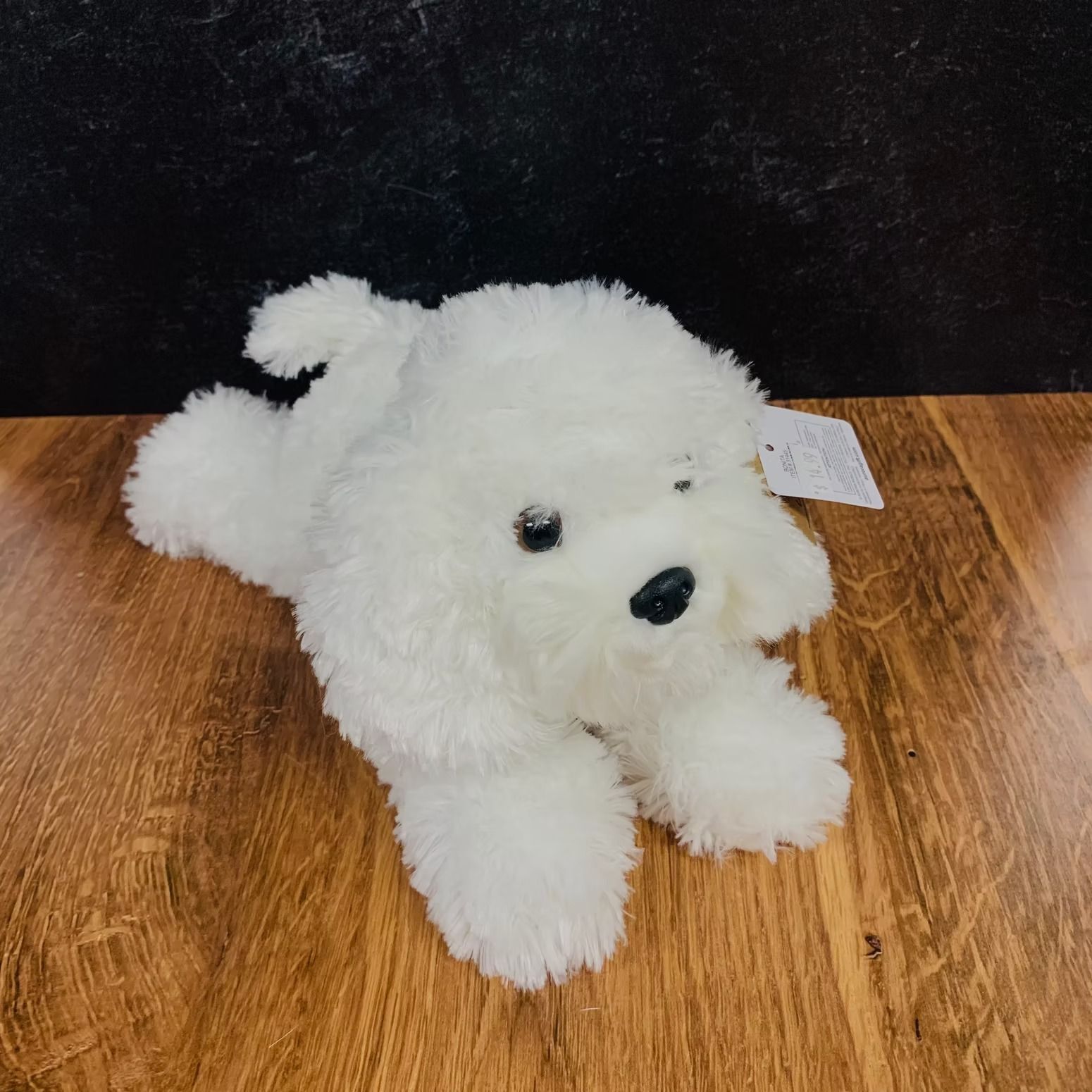 White plush dog lying down on a wood surface.
