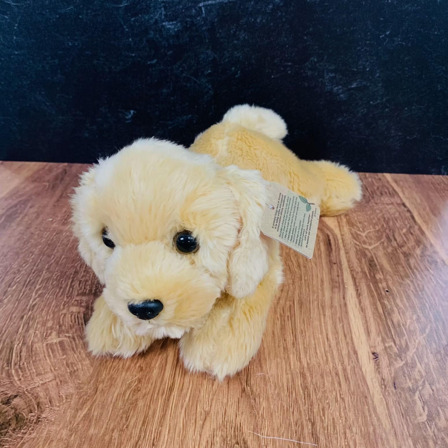 Golden retriever puppy plush toy lying on a wood surface.