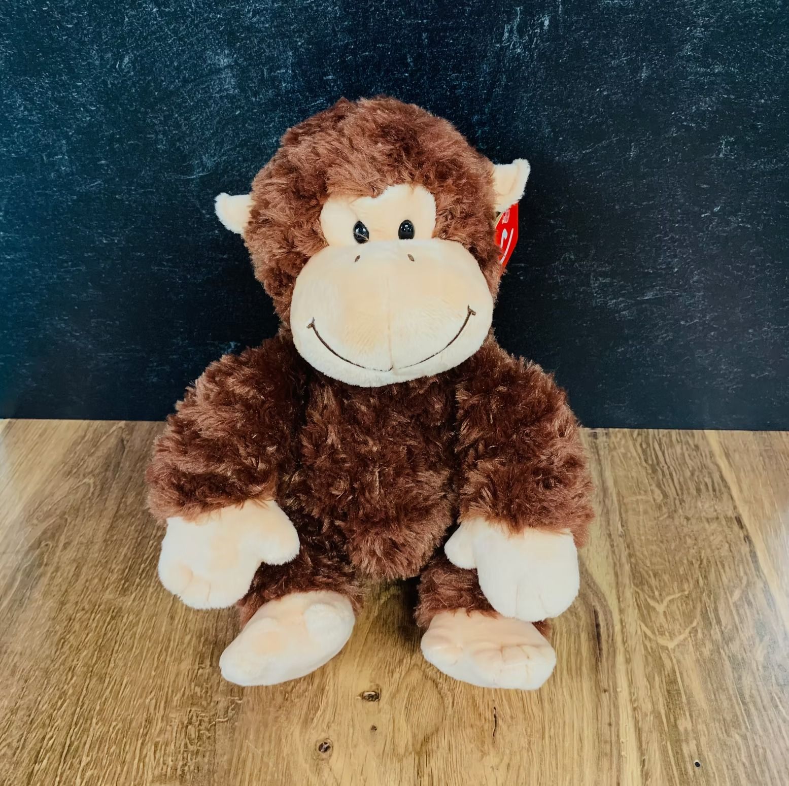Brown plush monkey with tan face, ears, hands, and feet sitting on a wooden surface.