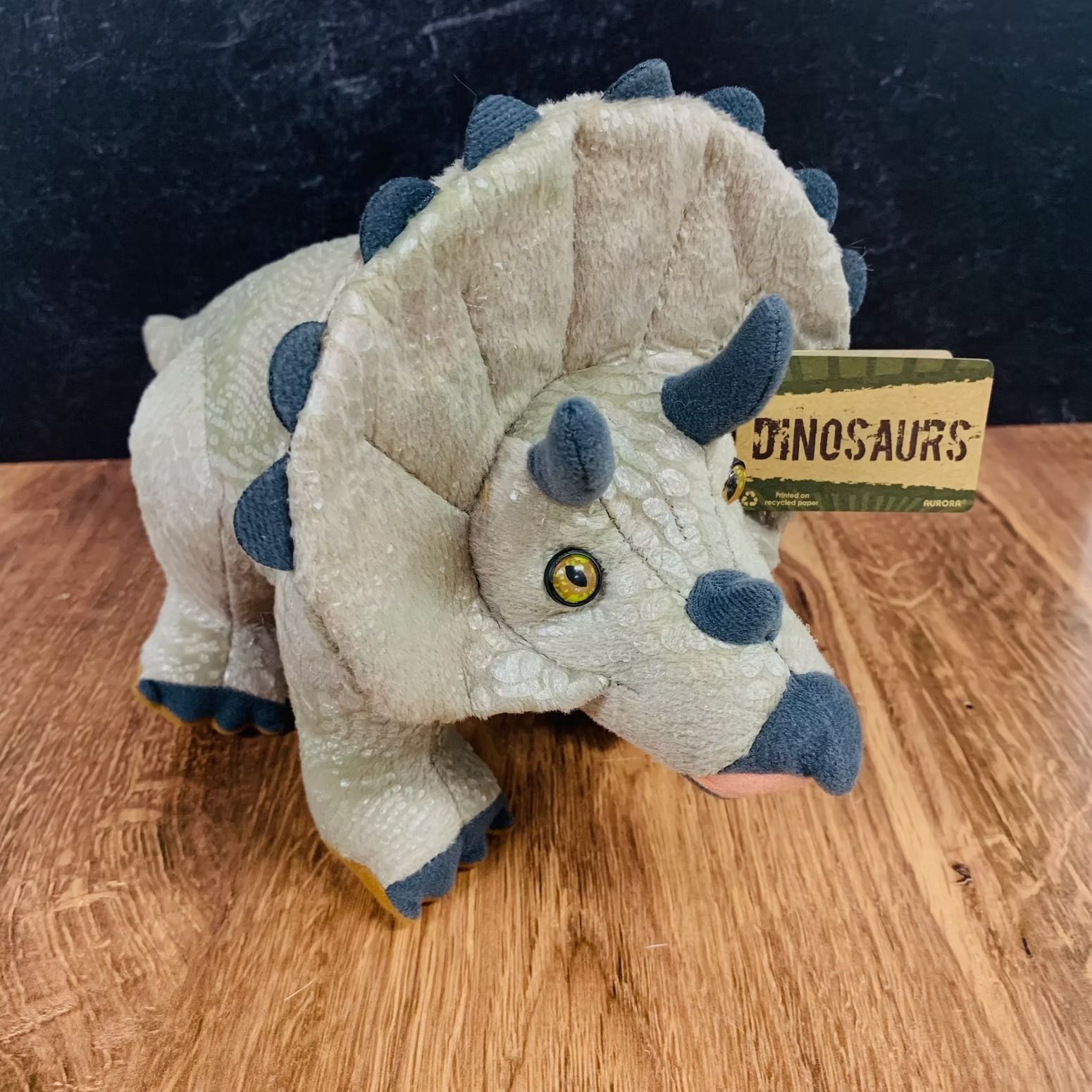 Plush toy triceratops with beige body, blue horns, and tag.
