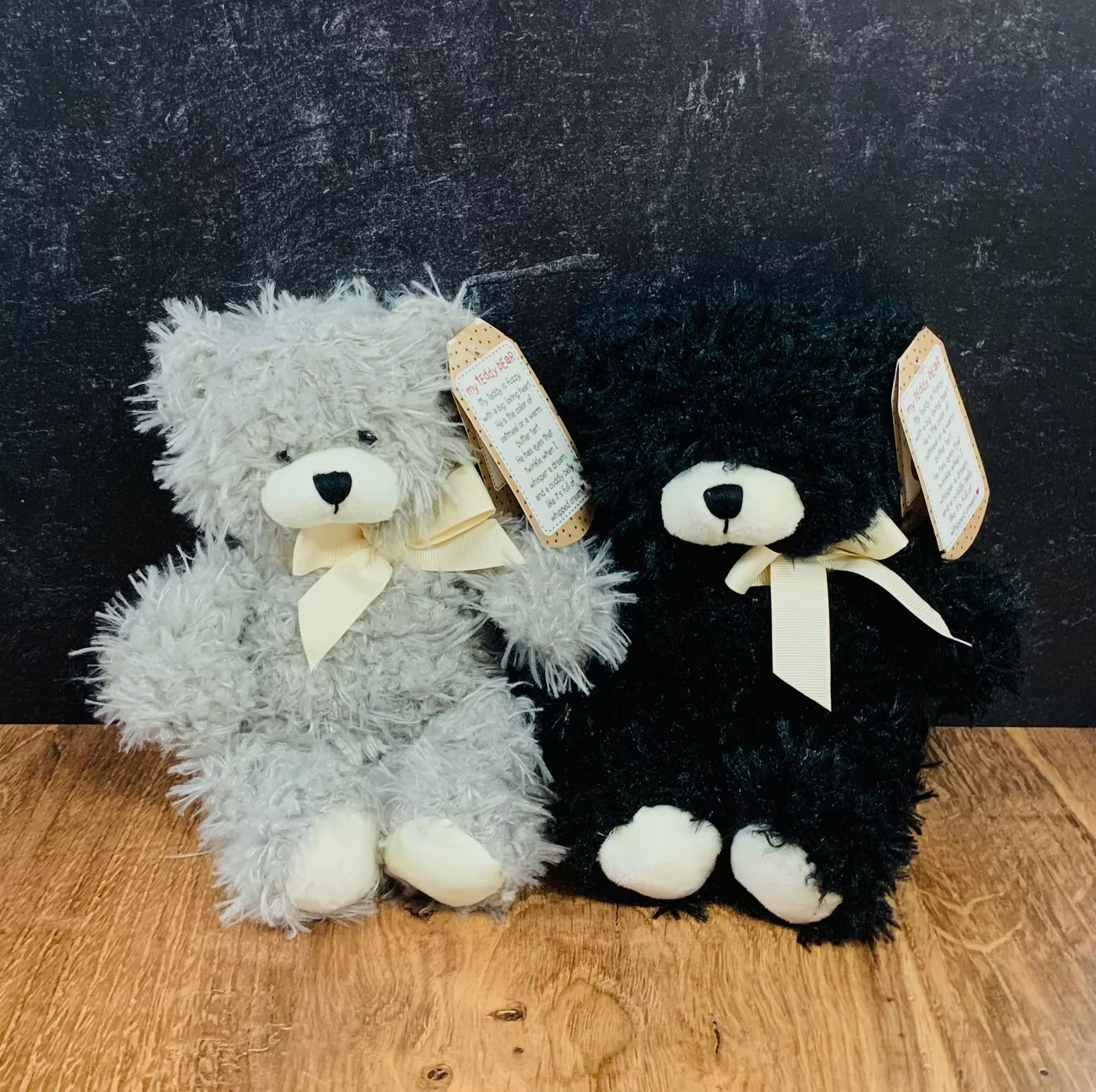 Two fluffy teddy bears, gray and black, with cream bows and tags, sitting side-by-side.