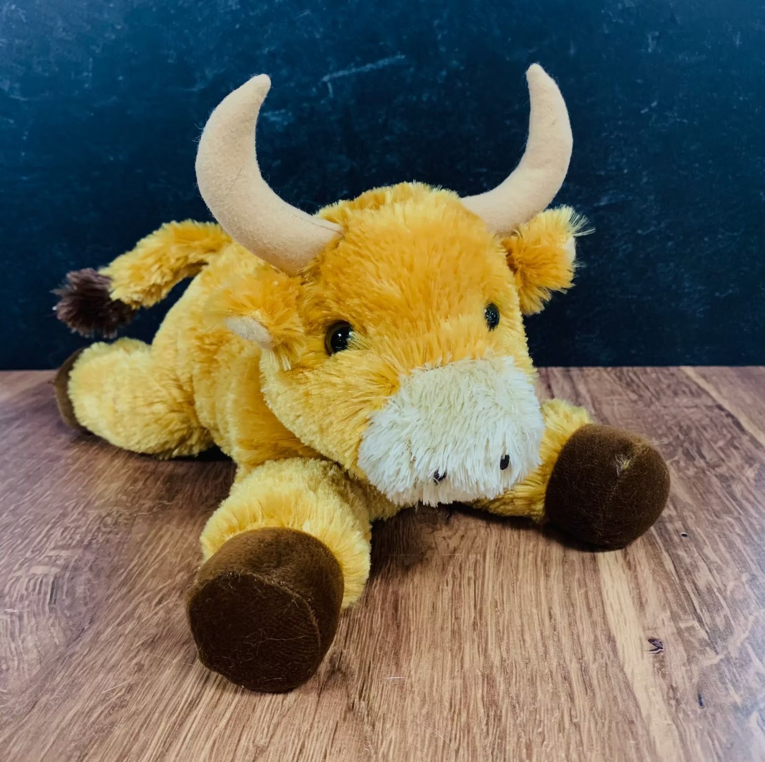Stuffed yellow bull with brown hooves and horns lying on wood.