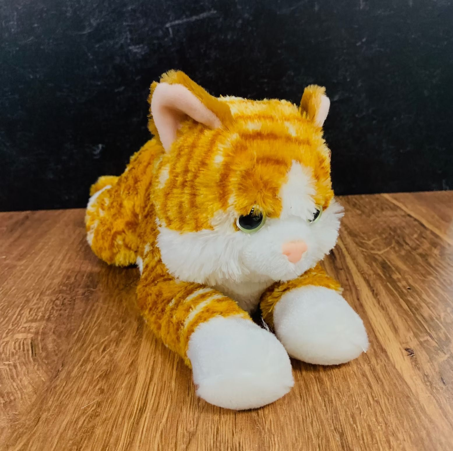 Orange and white tabby cat plush toy on wooden surface.