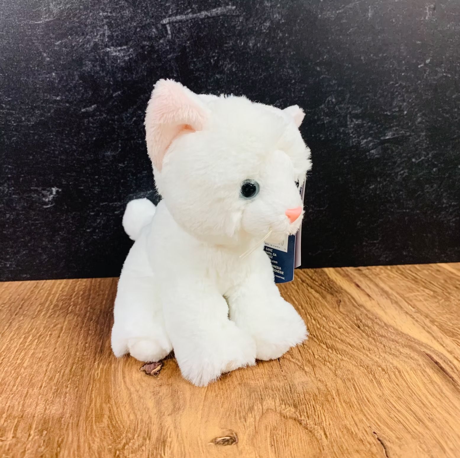White plush cat toy with pink ears and nose sitting on a wooden surface.