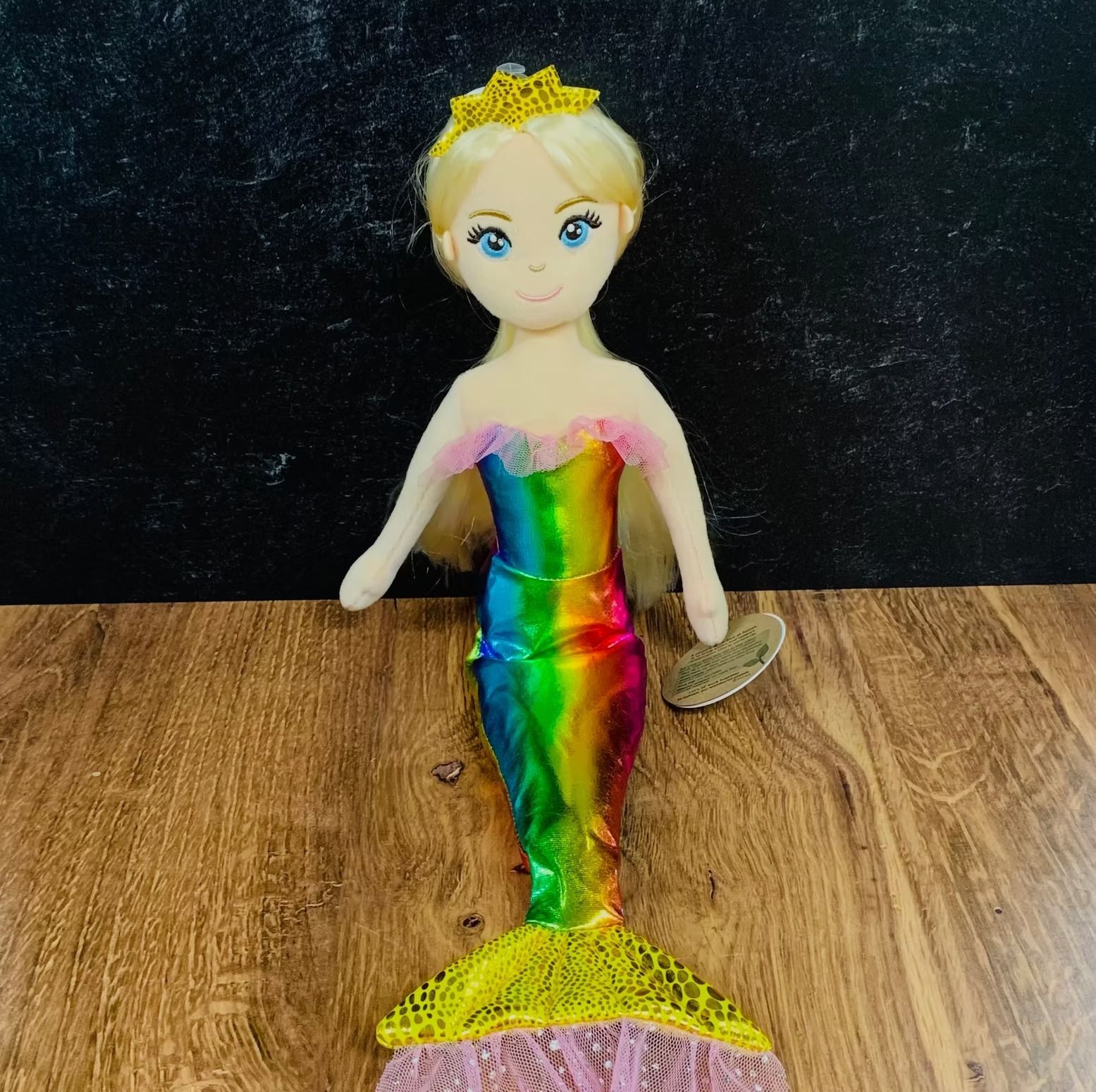 Mermaid doll with rainbow tail, blonde hair, golden crown, on wooden surface.