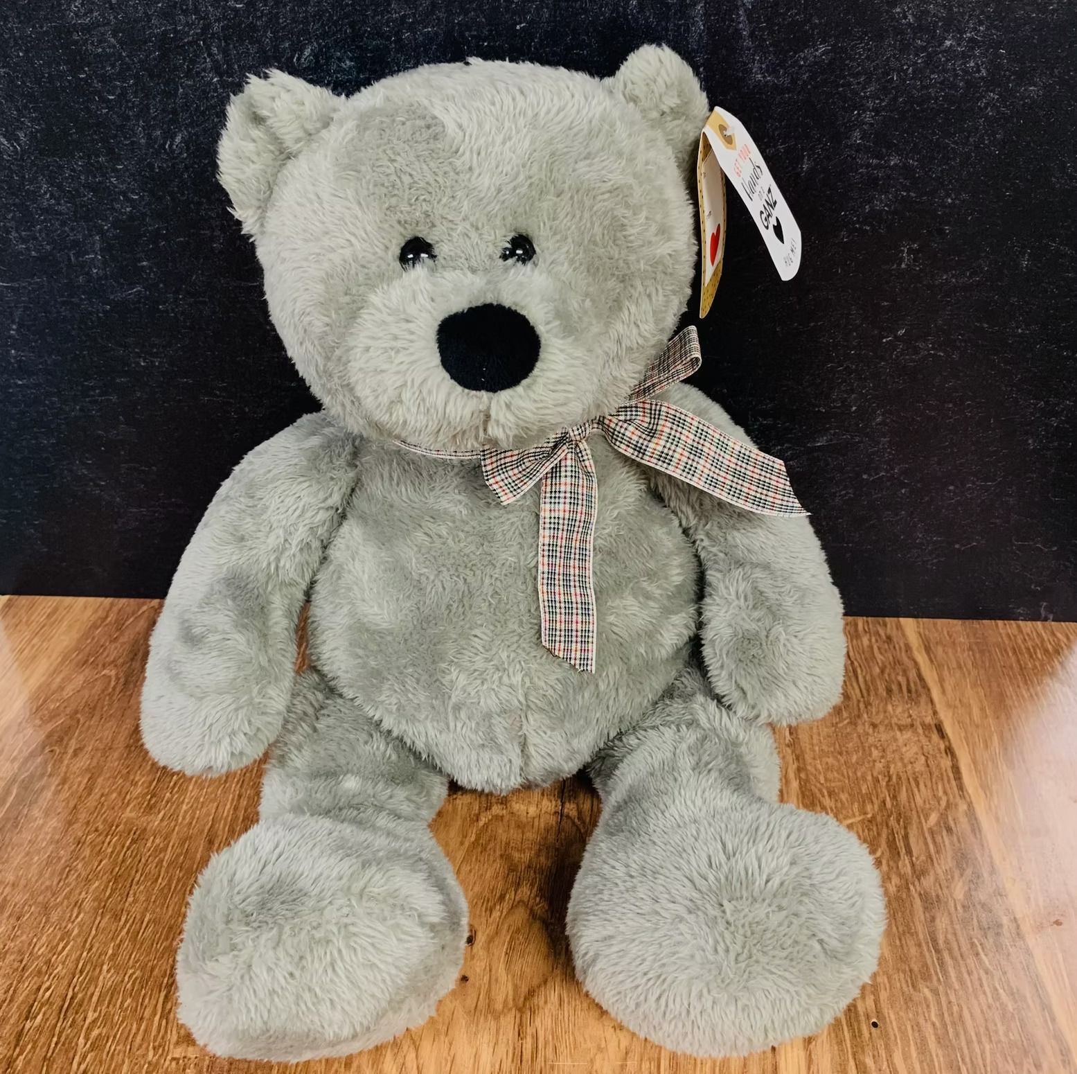Gray plush teddy bear with a patterned ribbon, on a wooden surface.
