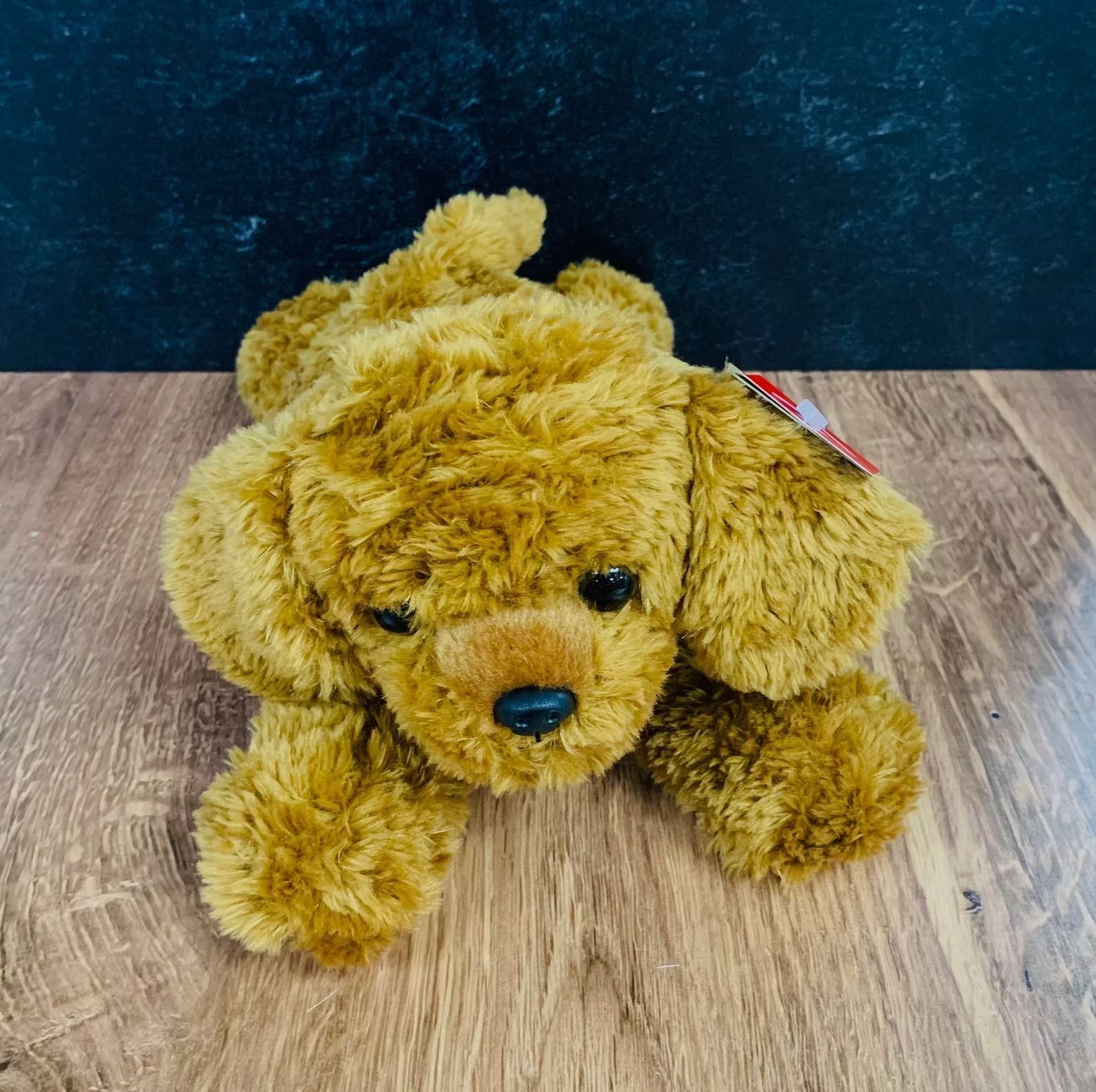 Brown plush dog toy lying on a wooden surface.