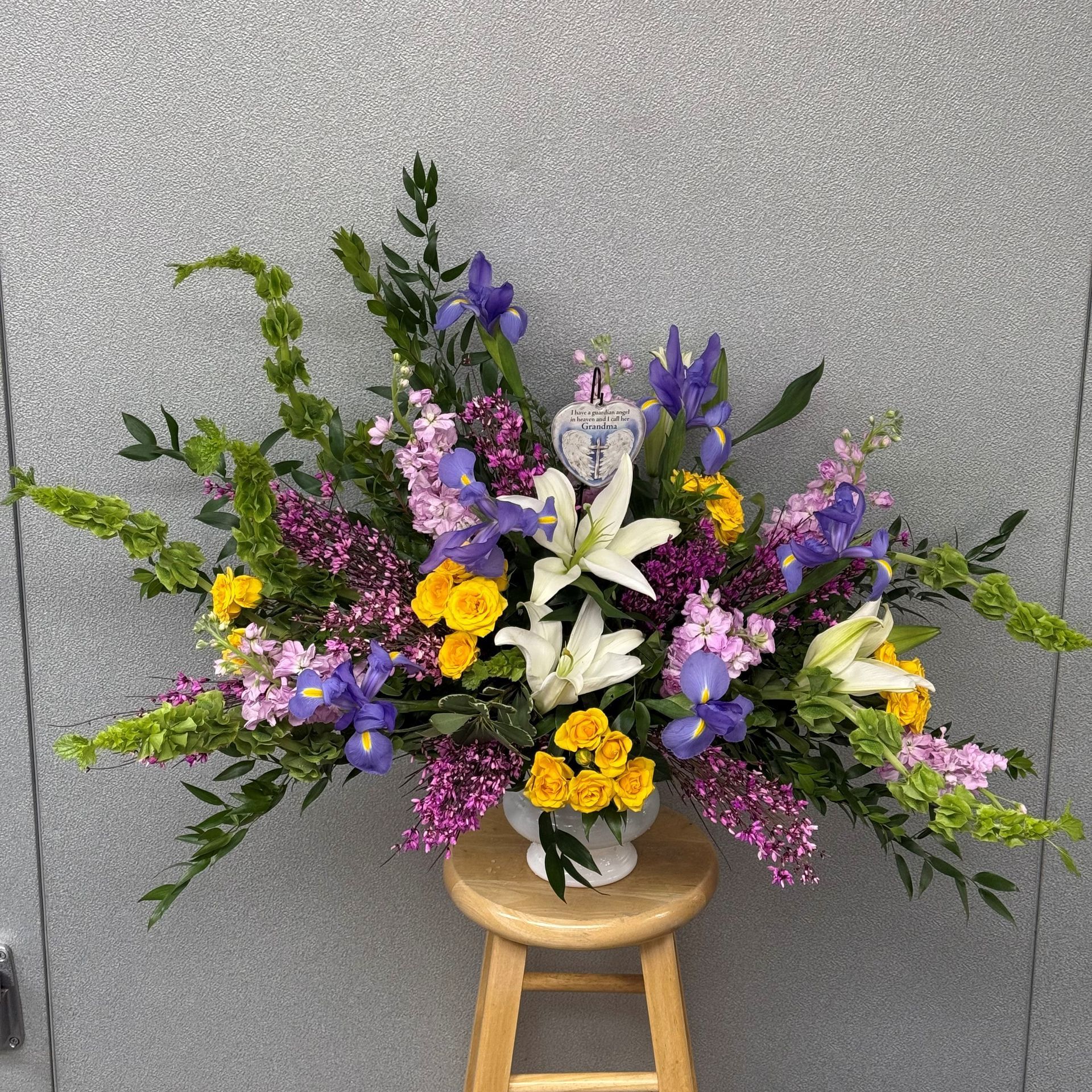 Floral arrangement with yellow, purple, and white flowers in a white vase on a stool.
