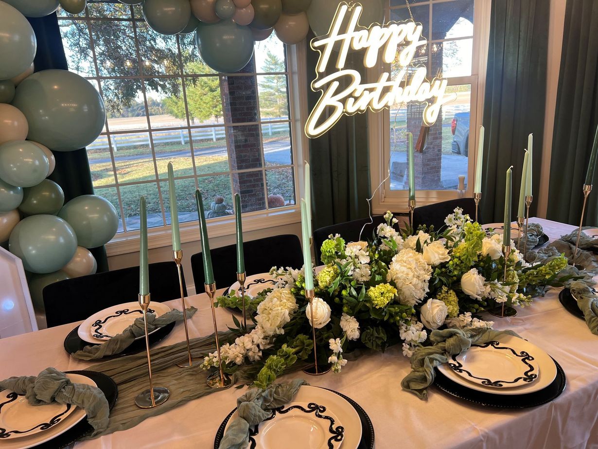 A table with plates, candles, flowers, and a neon sign that says 'Happy Birthday.'