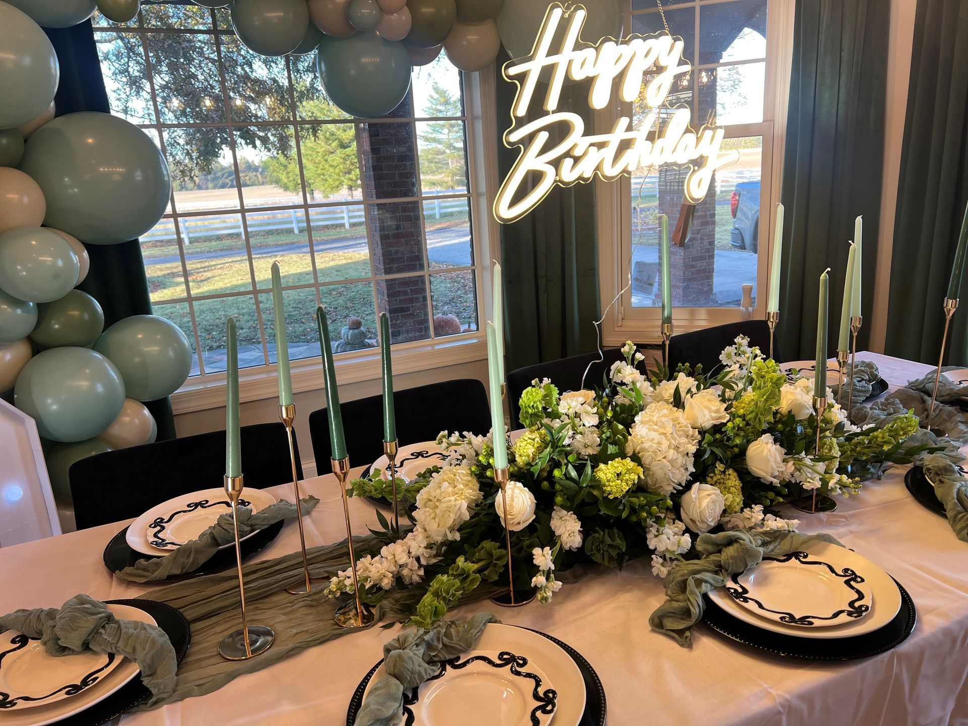 Birthday table setting with white and green floral centerpiece, candles, and balloons.