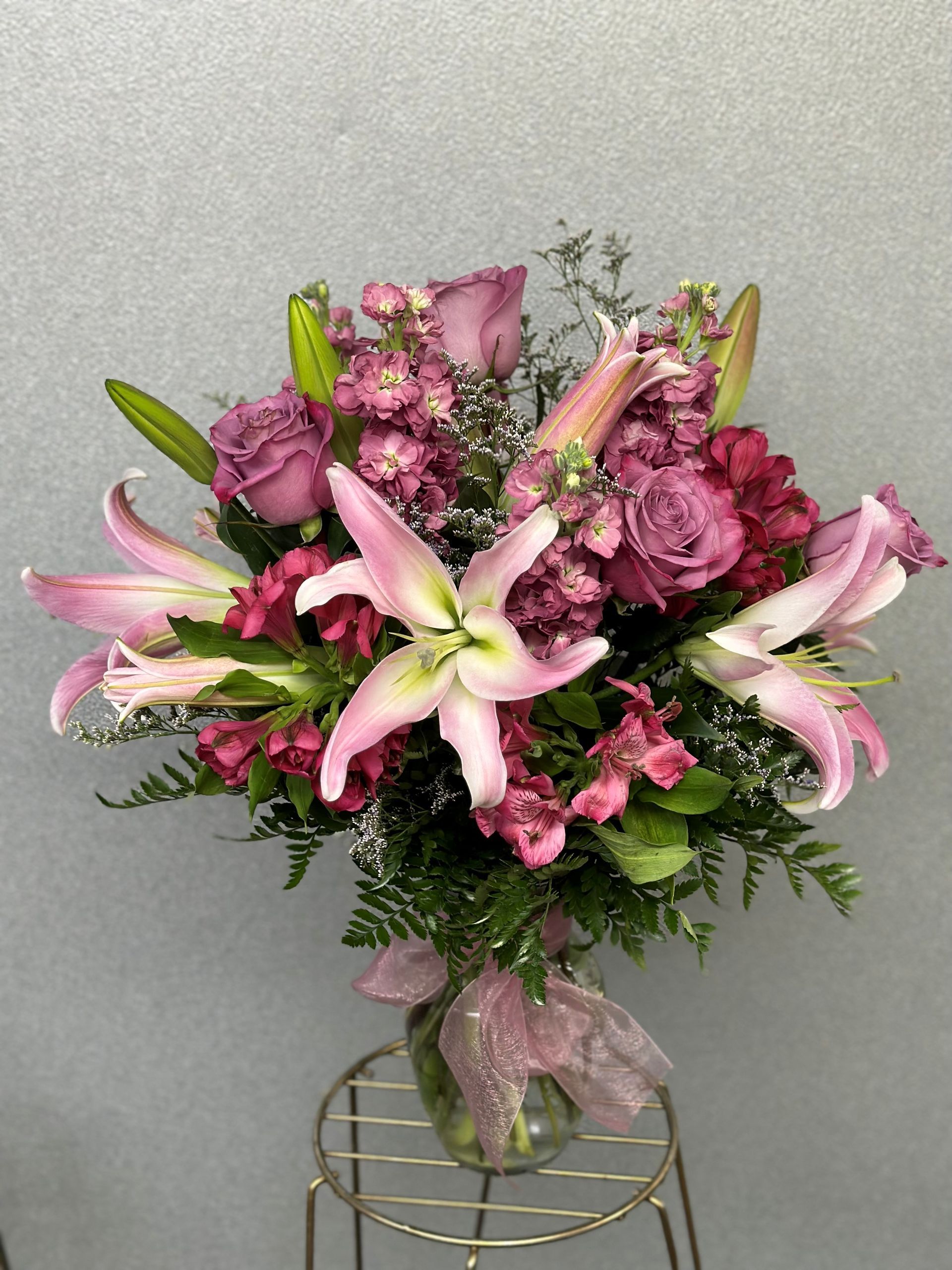 Pink lilies and roses in a glass vase, on a gold stand.