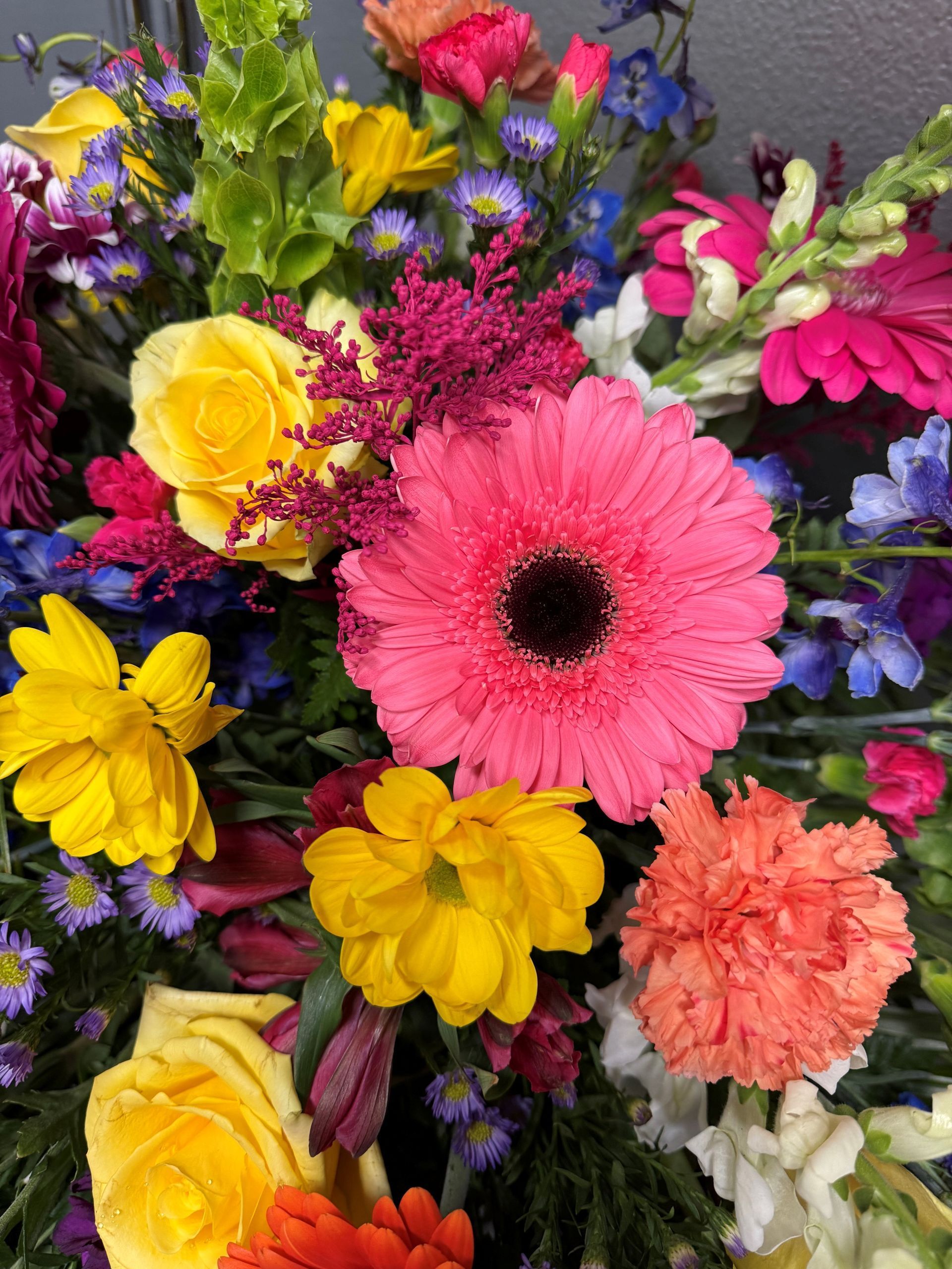 Vibrant bouquet of pink gerbera daisy, yellow roses, and mixed colorful flowers.