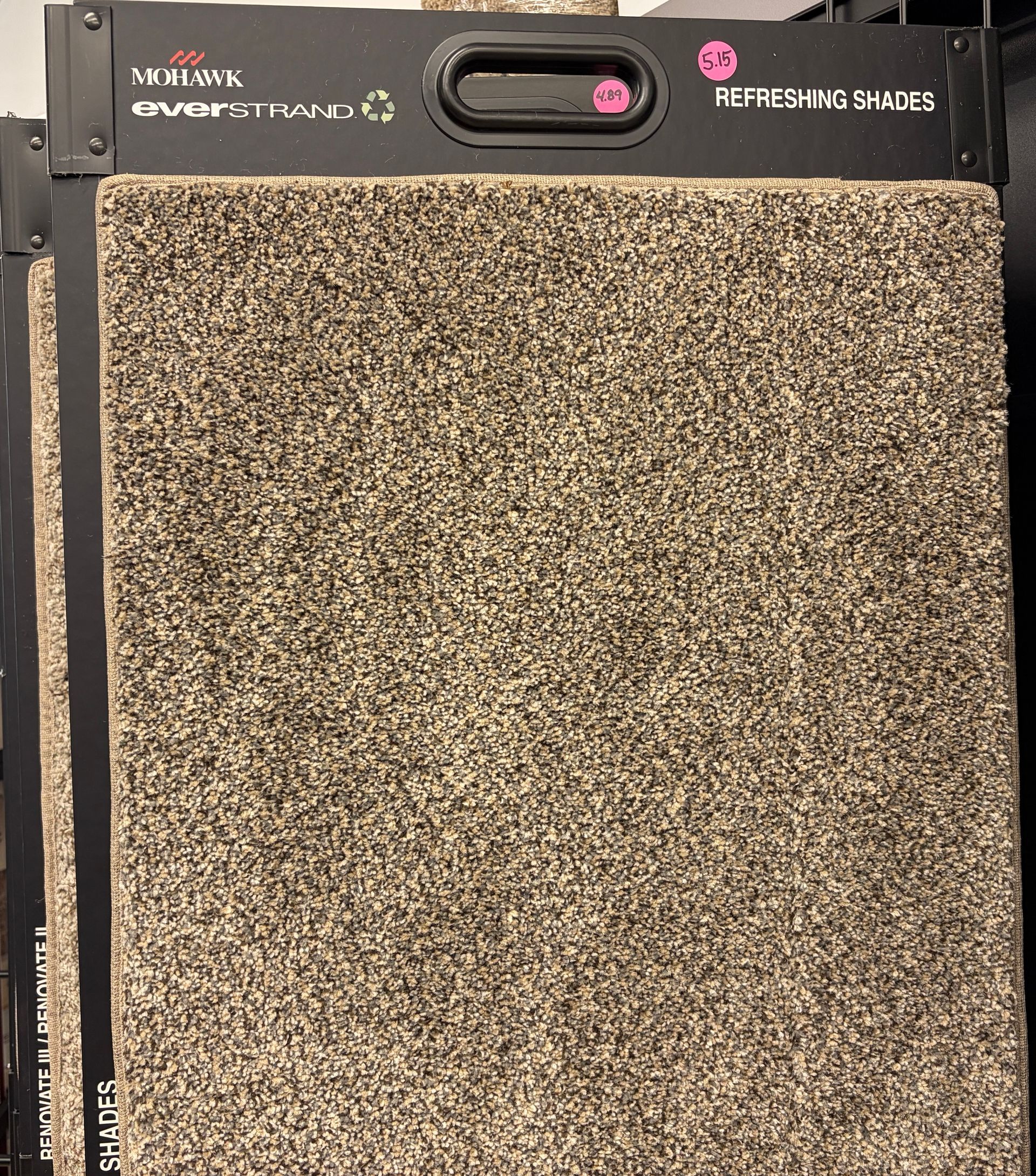 Carpet sample in beige and brown tones, displayed on a black rack.